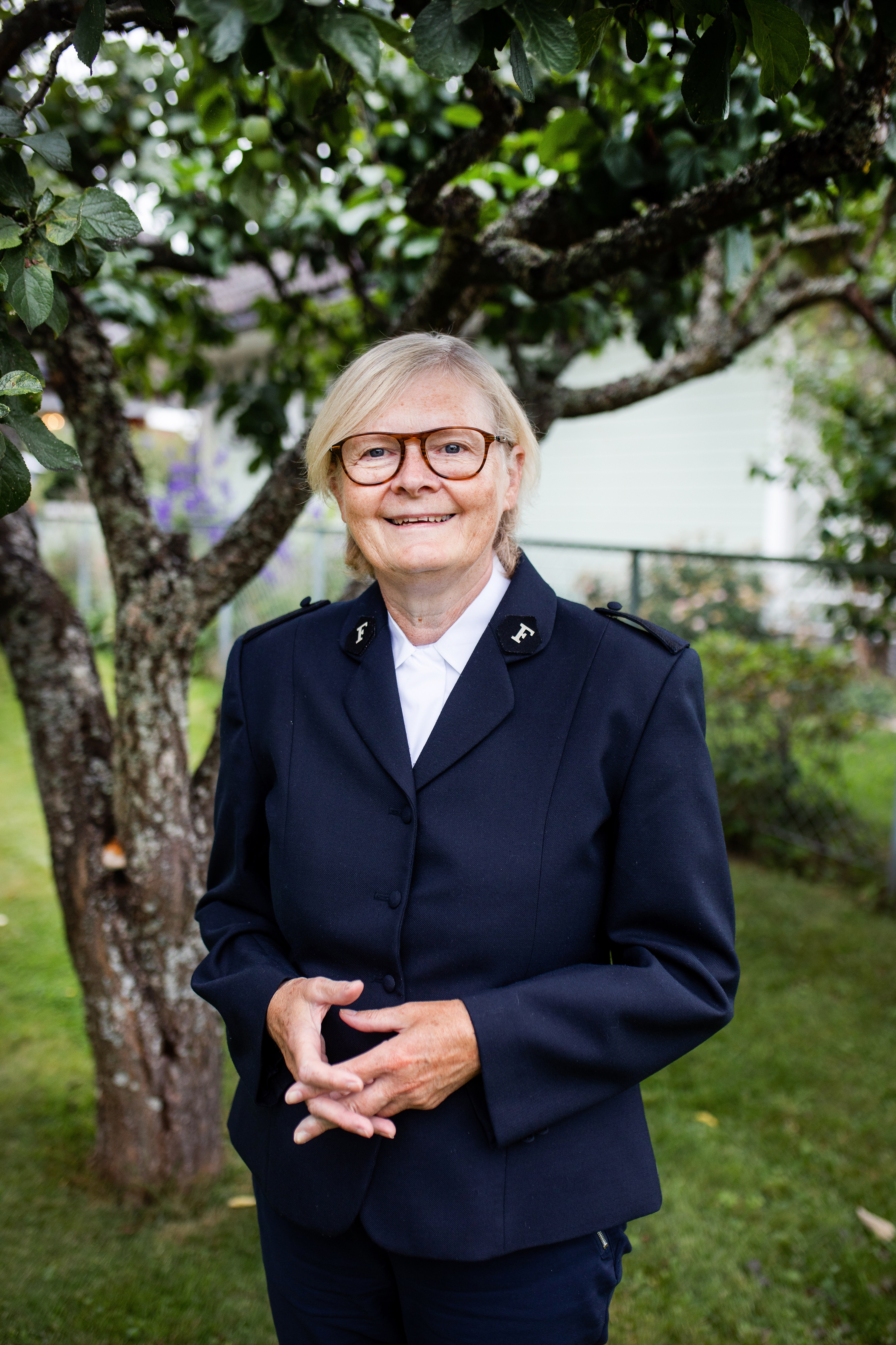 Sosialsjef i Frelsesarmeen Sosialsjef i Frelsesarmeen, Lindis Evja avbildet smilende i uniform i en grønn hage.