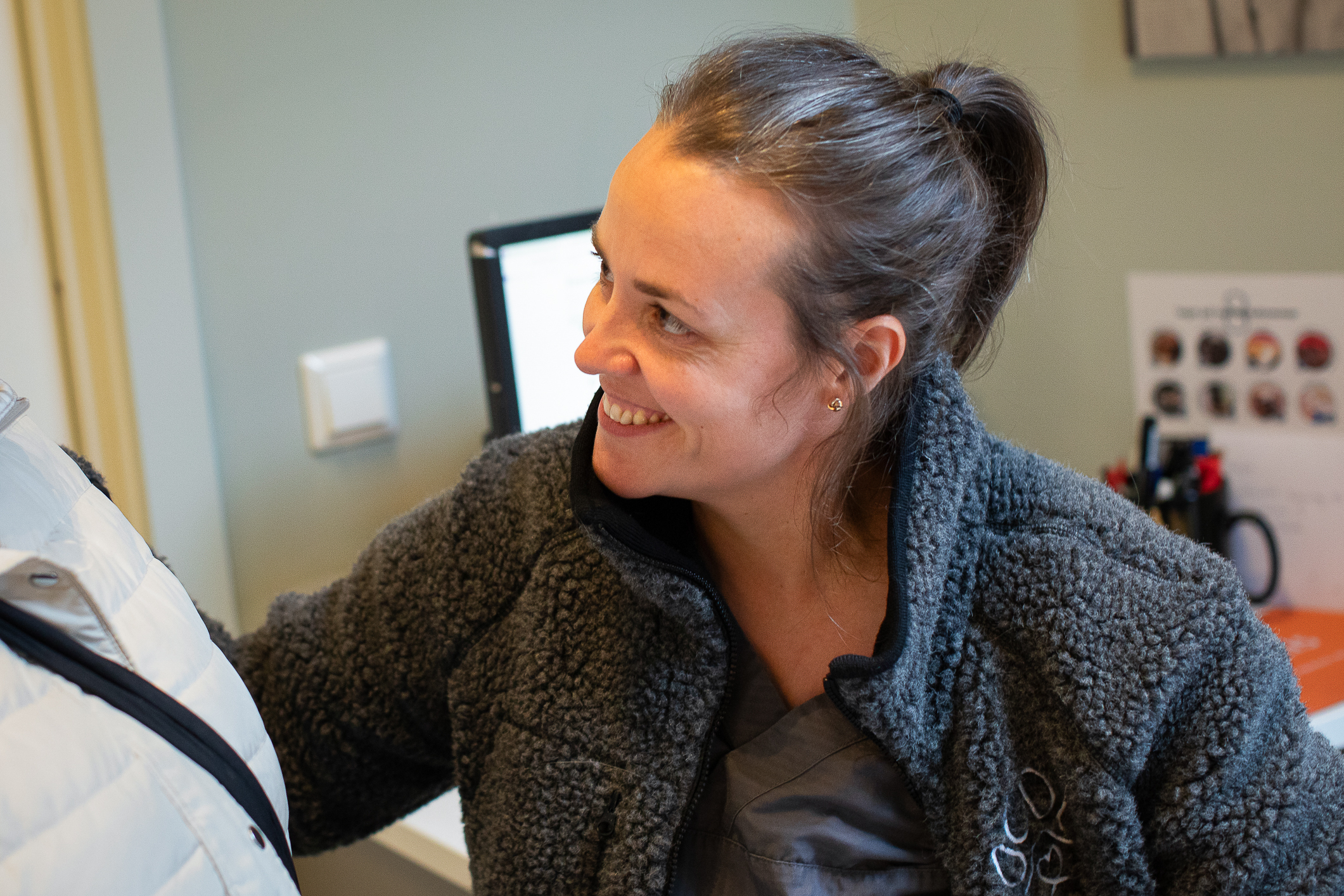 Kvinne med mørkt hår og hestehale smile og klapper et dyr som eieren holder.