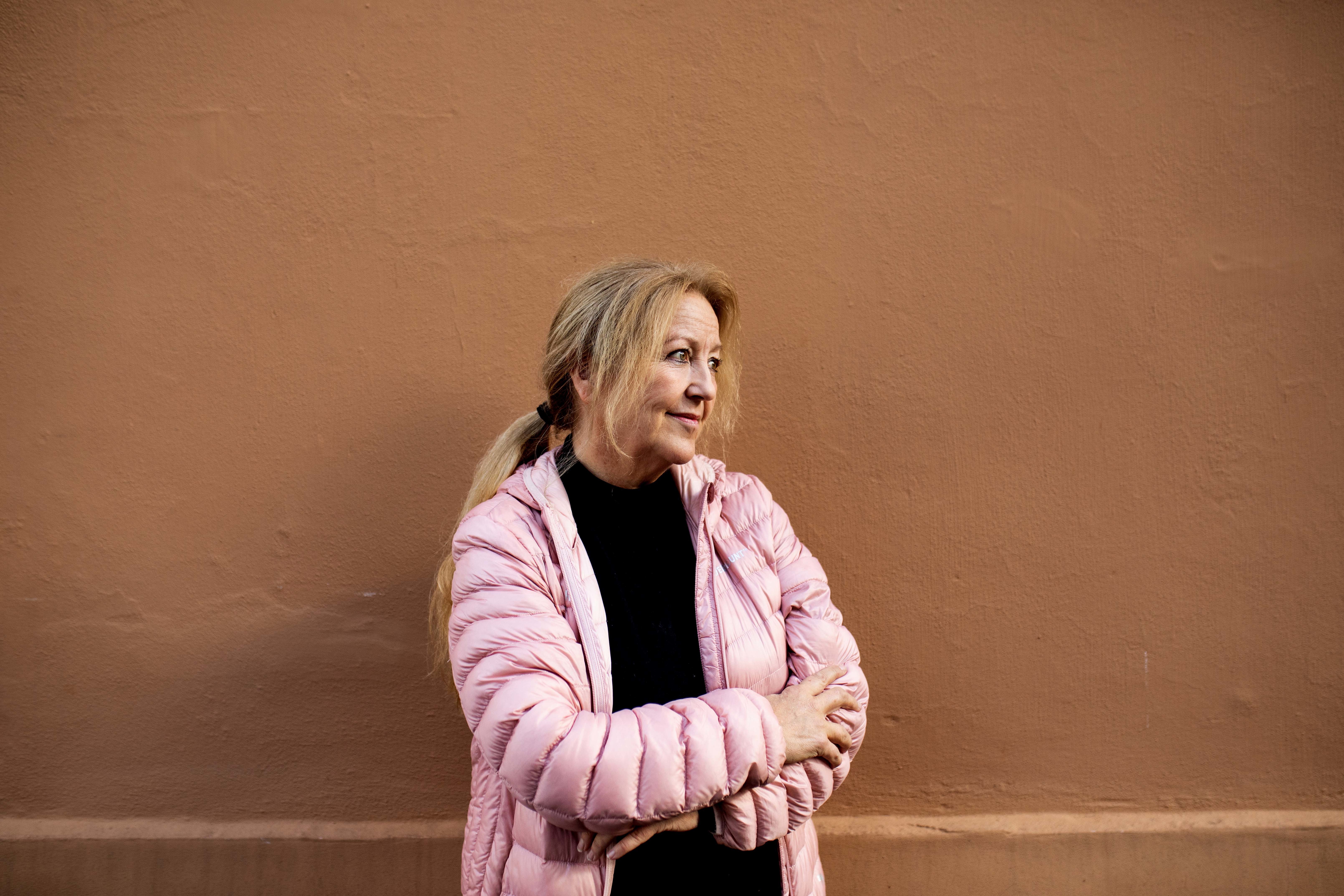 Lovise Angen Krogstad i sort høyhalset genser og rosa boblejakke står mot en teracotta farget murvegg
