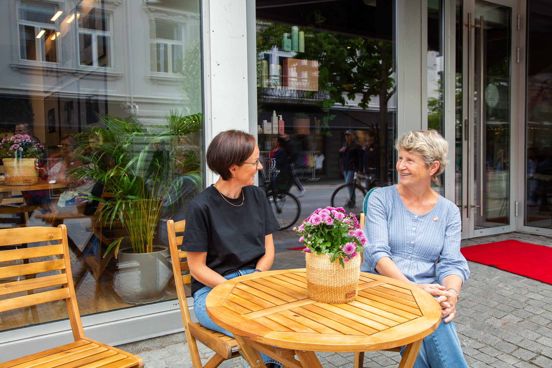 To kvinner sitter utenfor en hyggelig kafé ved et rundt trebord.