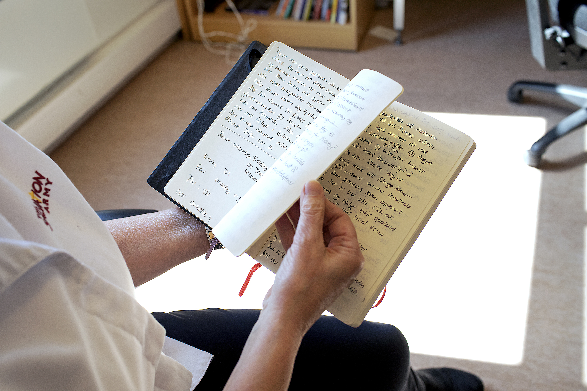 Bildet er et nærbilde av hendene til Marti, hun holder en oppslått notatbok med sider tettskrevet med notater.