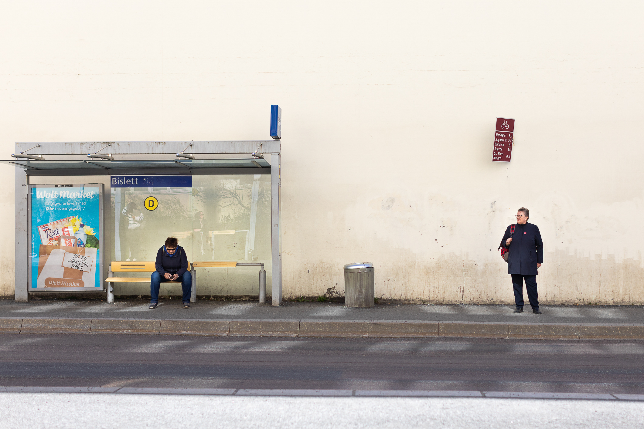 Eldre kvinne med briller og blå jakke med Frelsesarmeens røde skjold på, står på bussholdeplassen på Bislett.