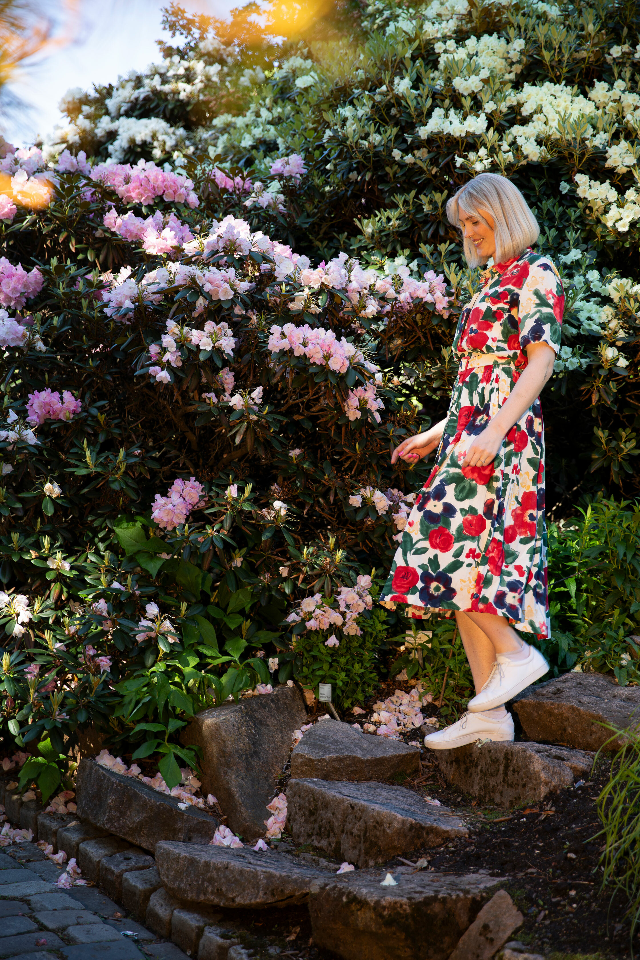 Foto: Ung kvinne i blomstrete kjole går ned en stientrap ute i en hage.