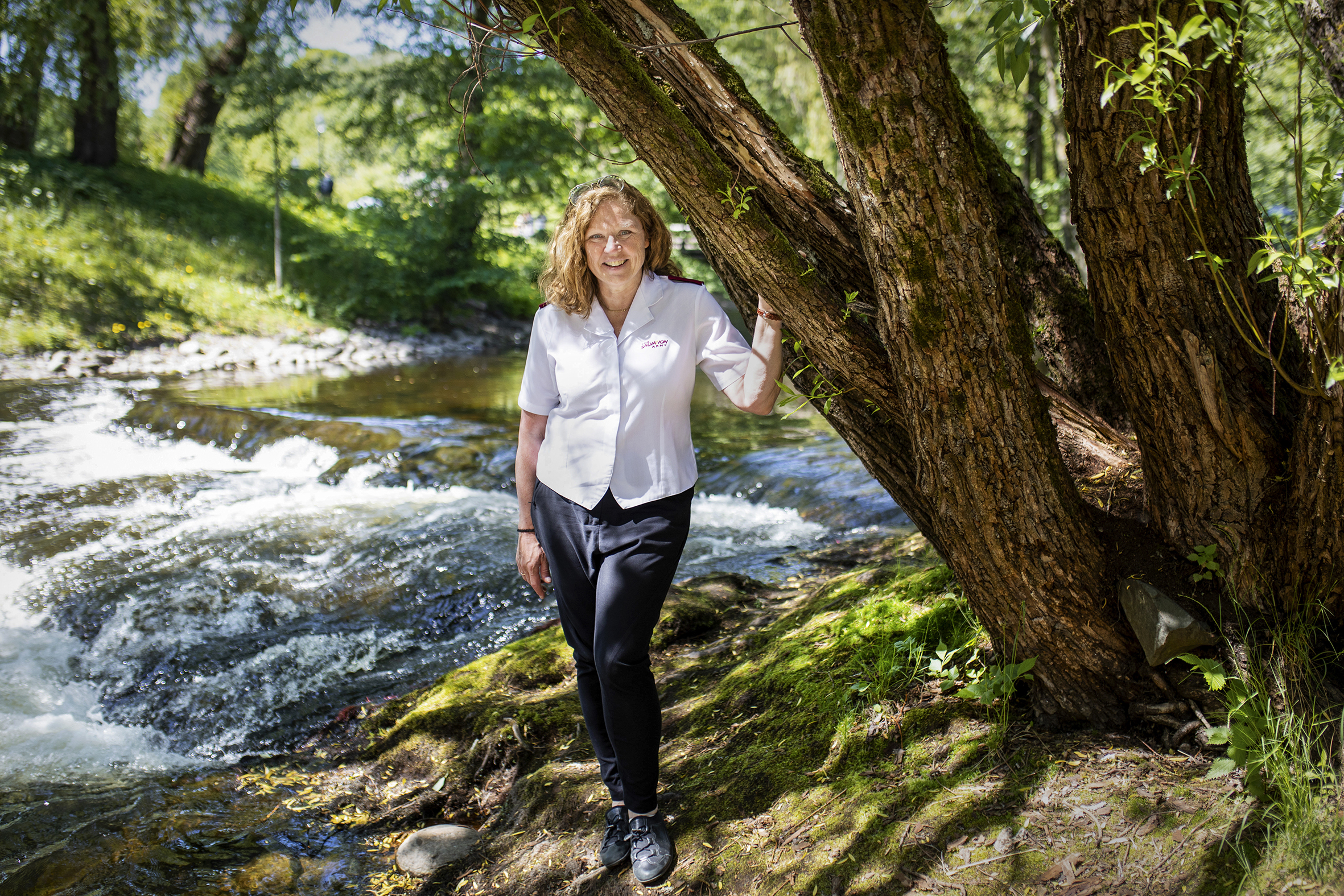 Marit Skartveit står foran noen trær og en elv og smiler til kamera