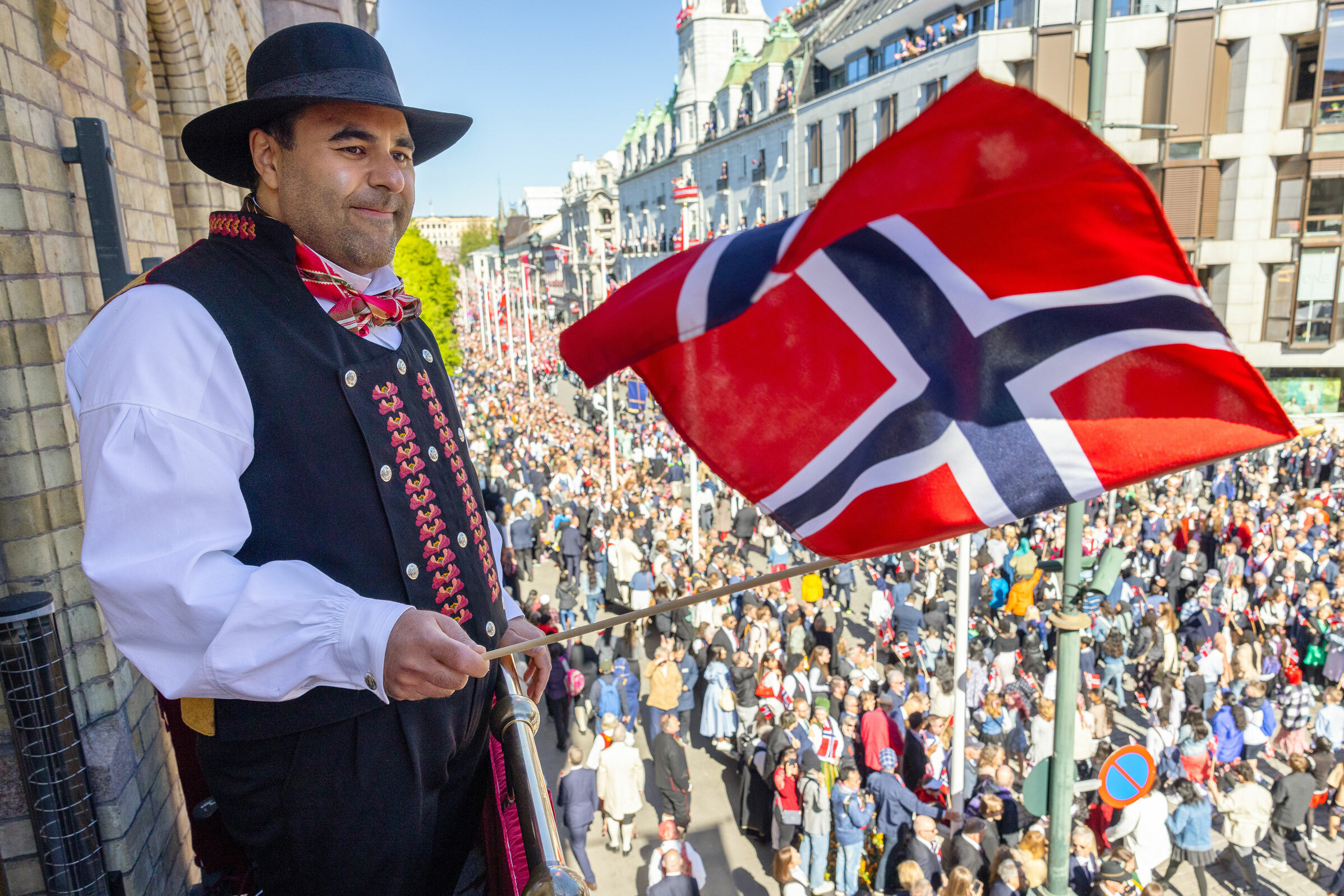 Foto: Mann fra iran i norsk bunad med norsk flagg. Han veiver flagget fra en balkong høyt over folkehavet.