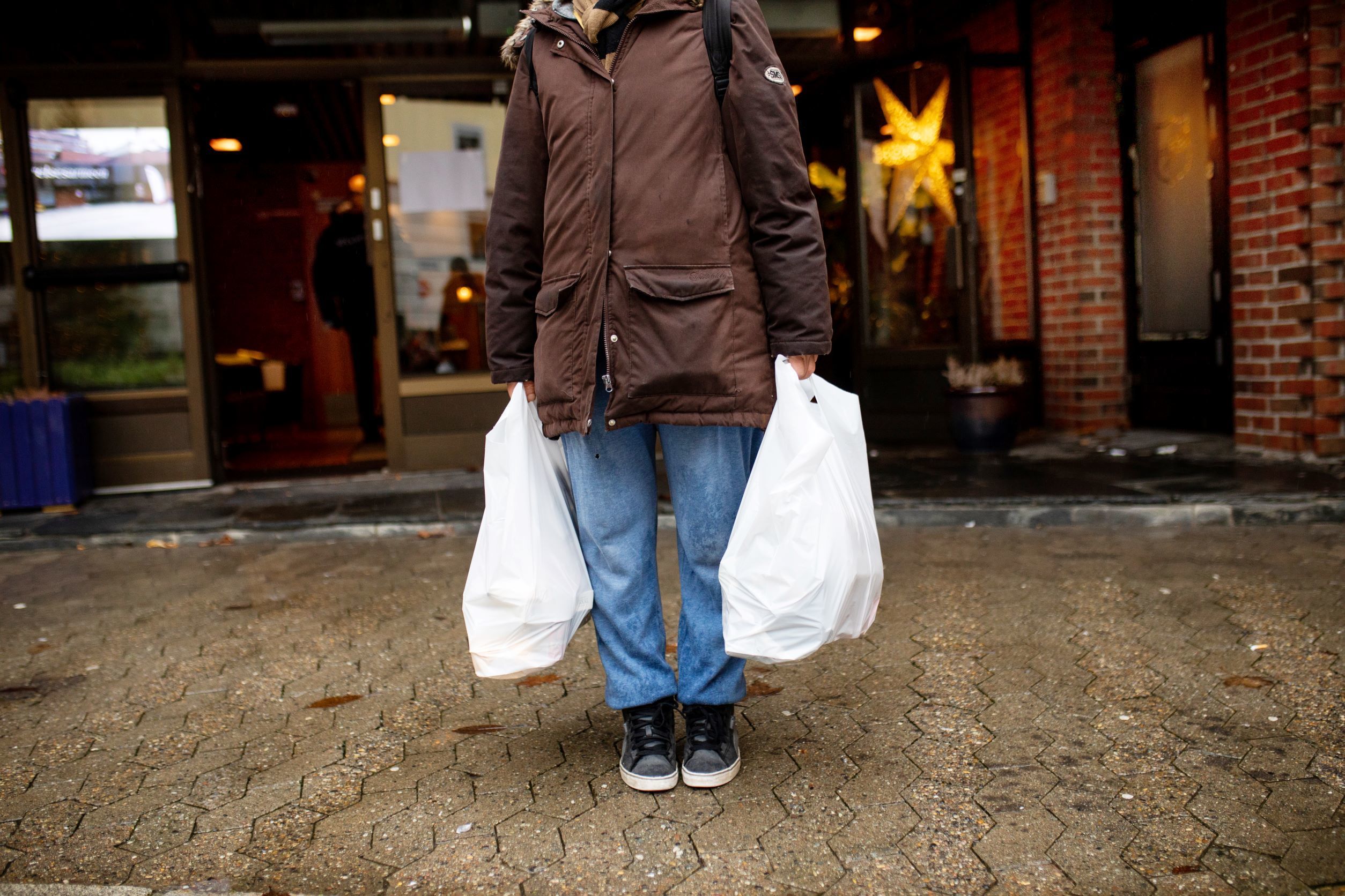 Person som bærer to bæreposer fulle med mat. Anonym, man ser kun fra livet og ned. En kasse med diverse mat.
