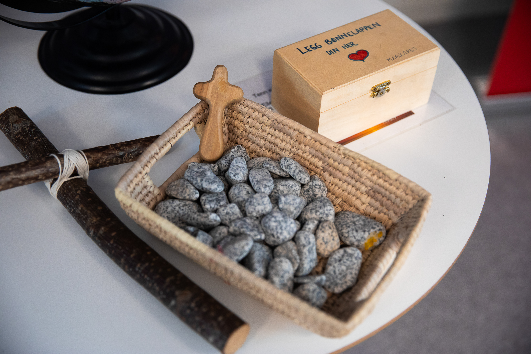 Foto: Nærbilde av korg med steiner, kors og en eske i tre der dolk kan legge bønnelapper.