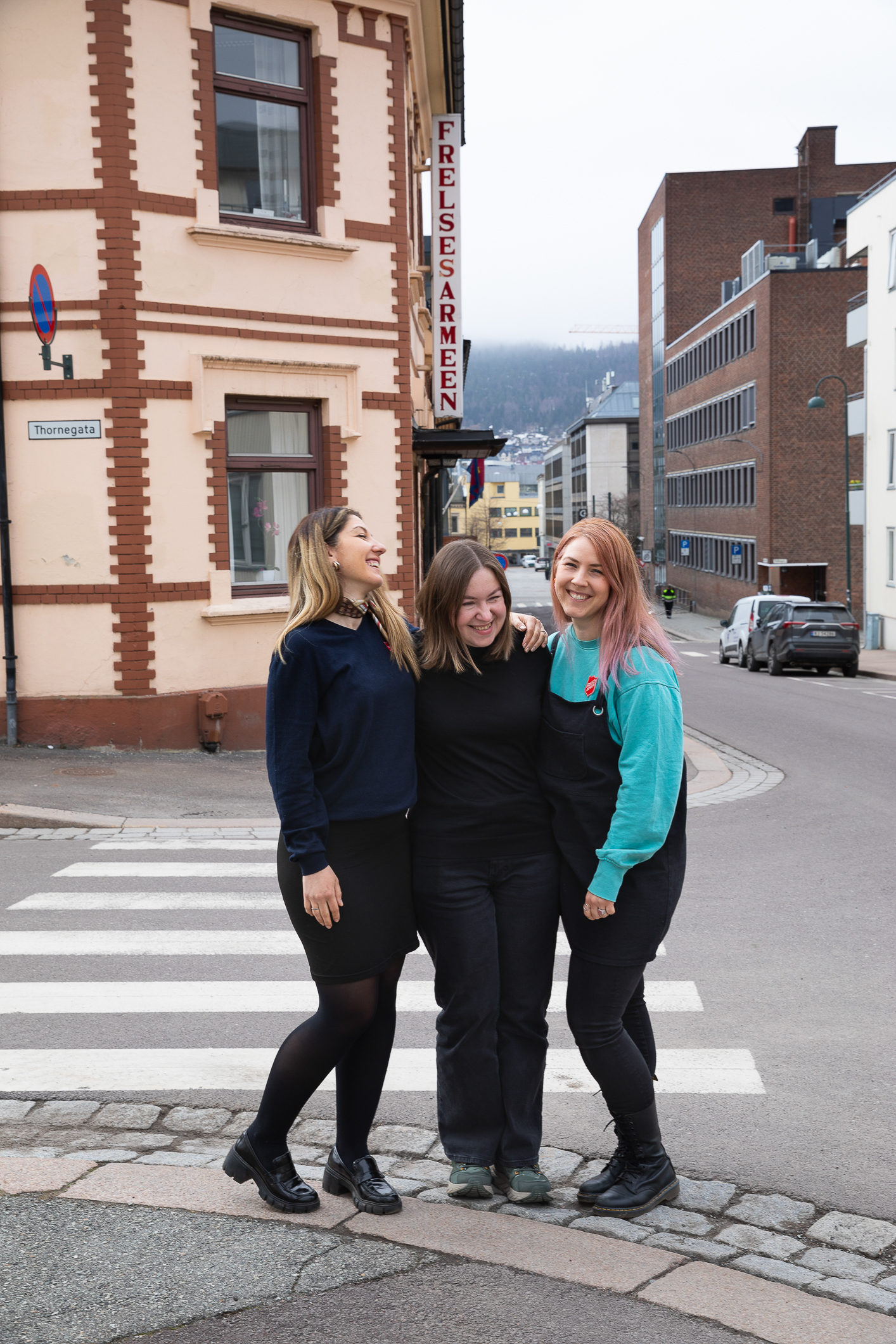 Foto: Tre kvinner står tett sammen i en klynge utenfor Frelsesarmeens bygg i Drammen. De klemmer hverandre og smiler.