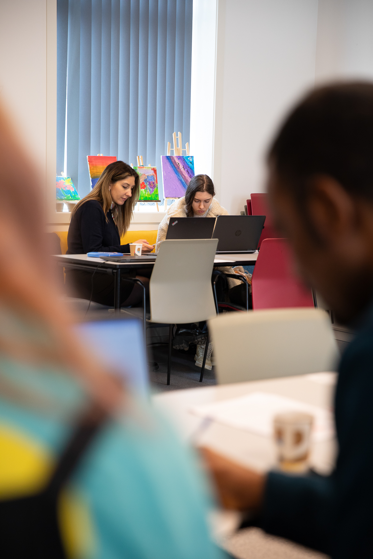 Foto: På avstand ser vi to kvinner ved siden av hverandre ved to PC-er.