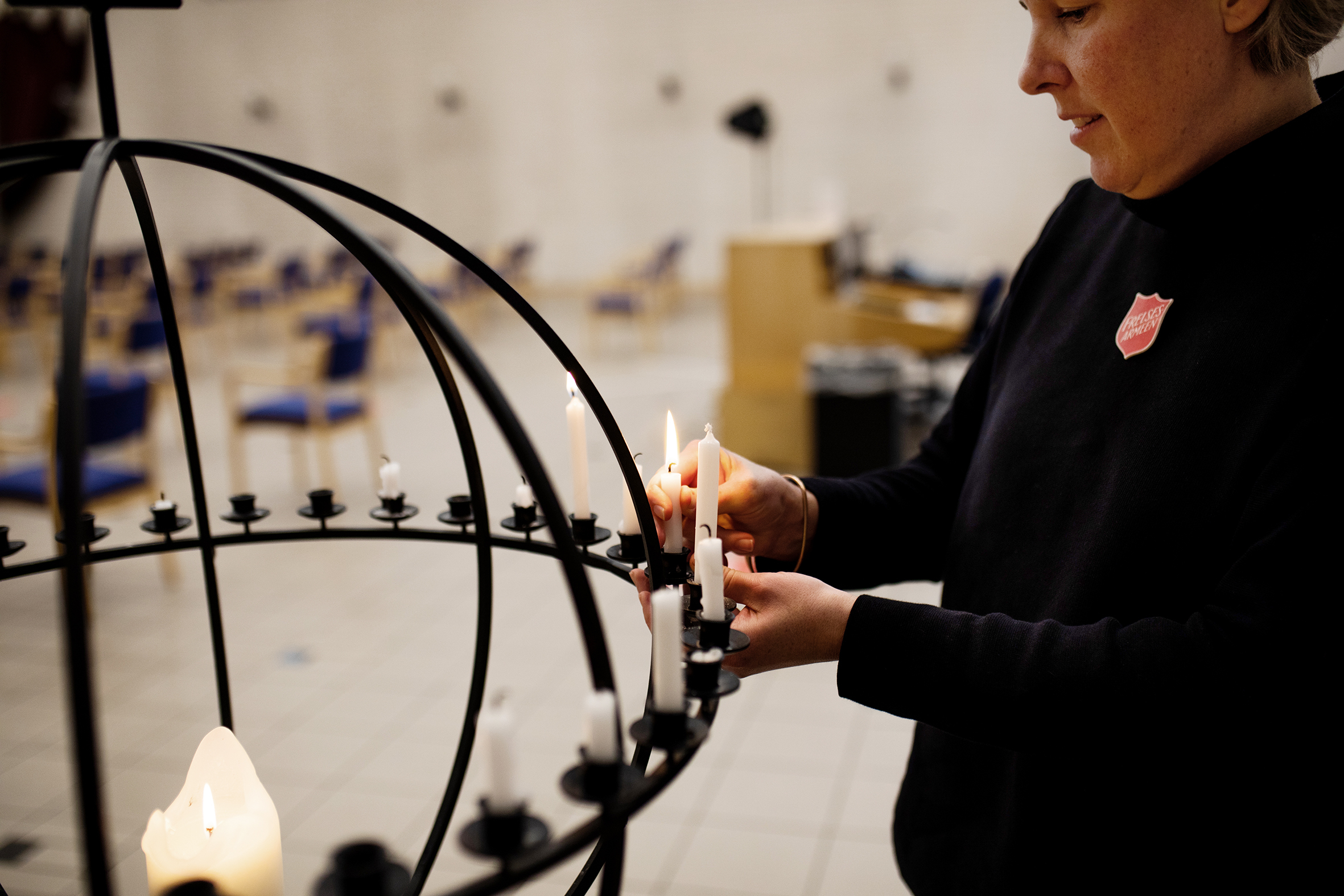 Bildet er tatt fra siden og viser kjellgren som står og tenner lys i en lysglobe av metall.