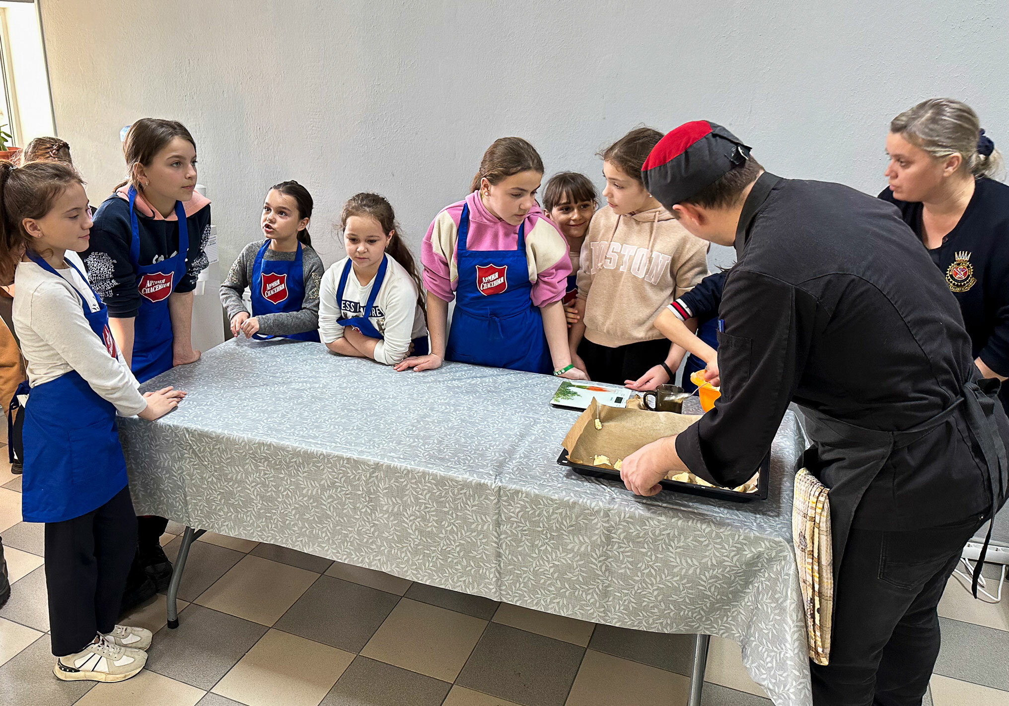 Foto: To voksne og mange barn står bøyd over et bord med duk.