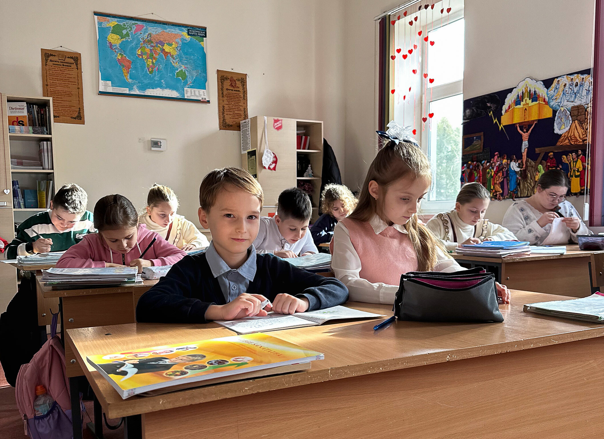 Foto: Ni barn i alderen 8 til 14 år sitter ved pulter i det som ligner et klasserom. De gjør lekser.