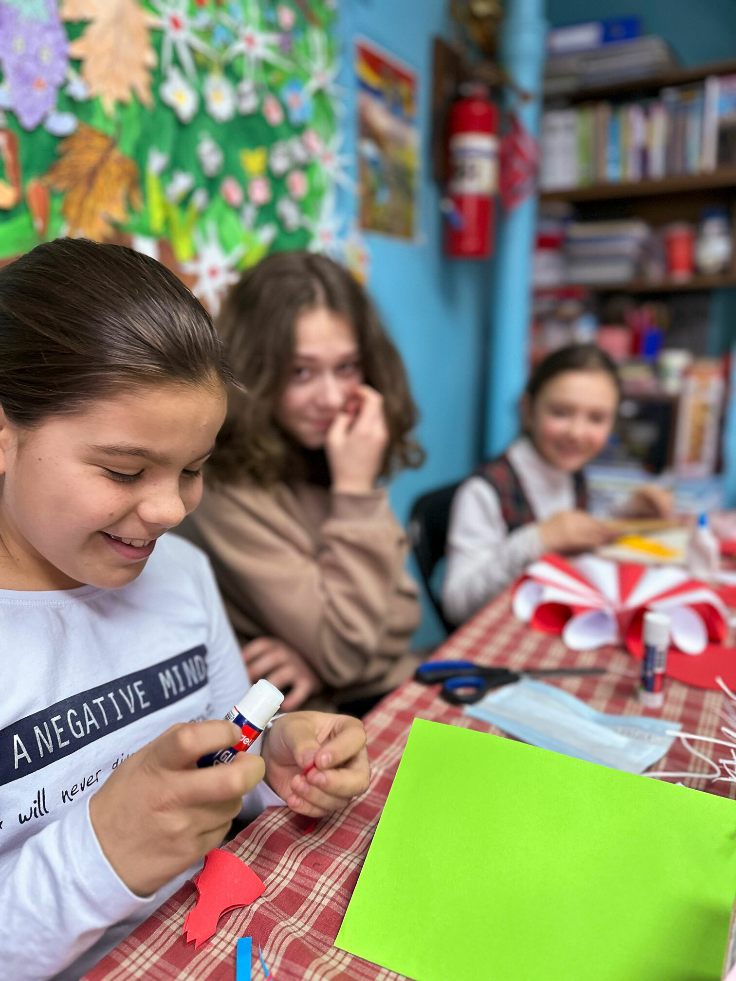 Foto: Tre jenter som holder på med hobbyaktiviteter. I bakgrunnen henger et fargerikt bilde.