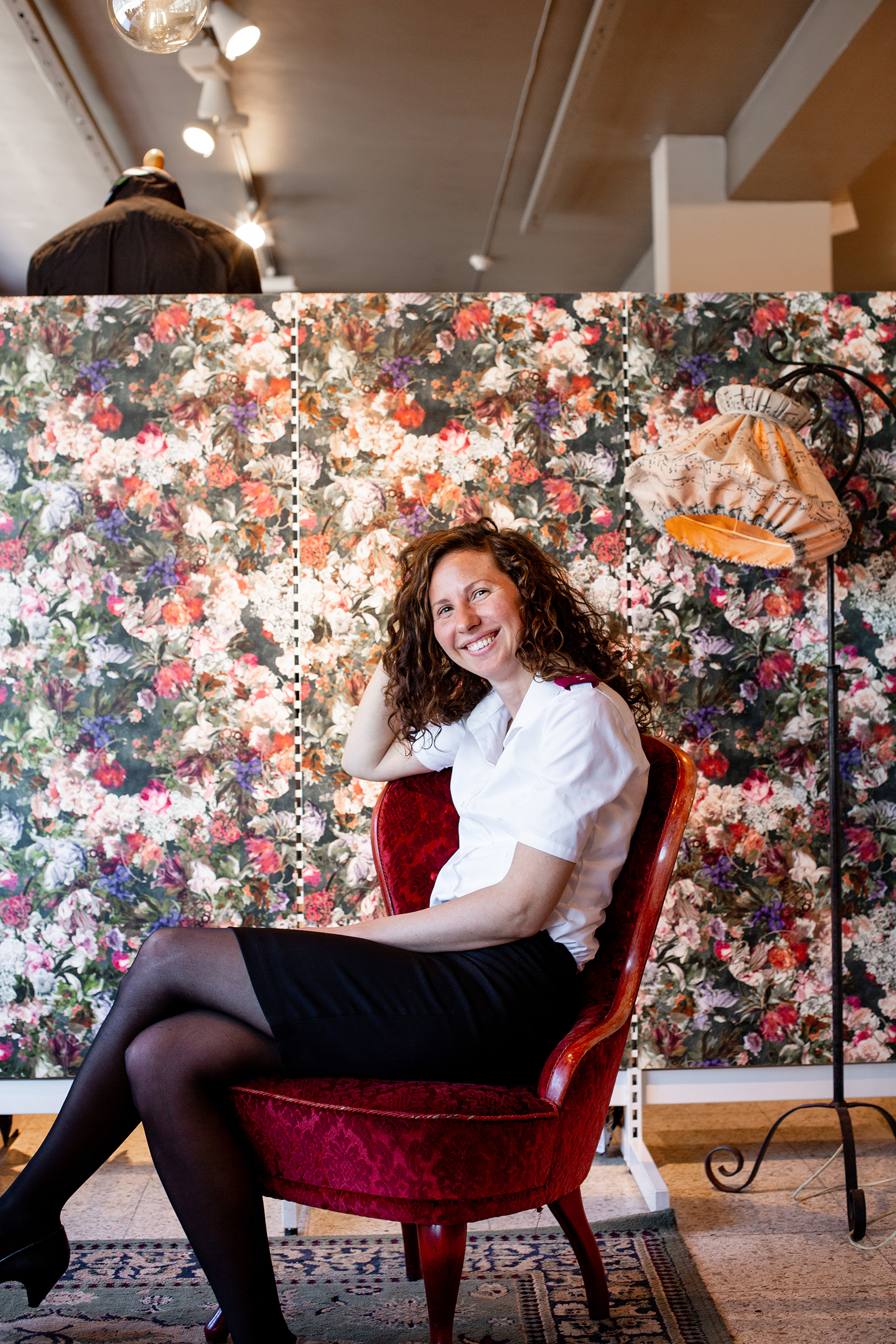 Monica har stort krøllete hår, Frelsesarmeen uniform og sitter i en rød stol foran en blomstrete vegg