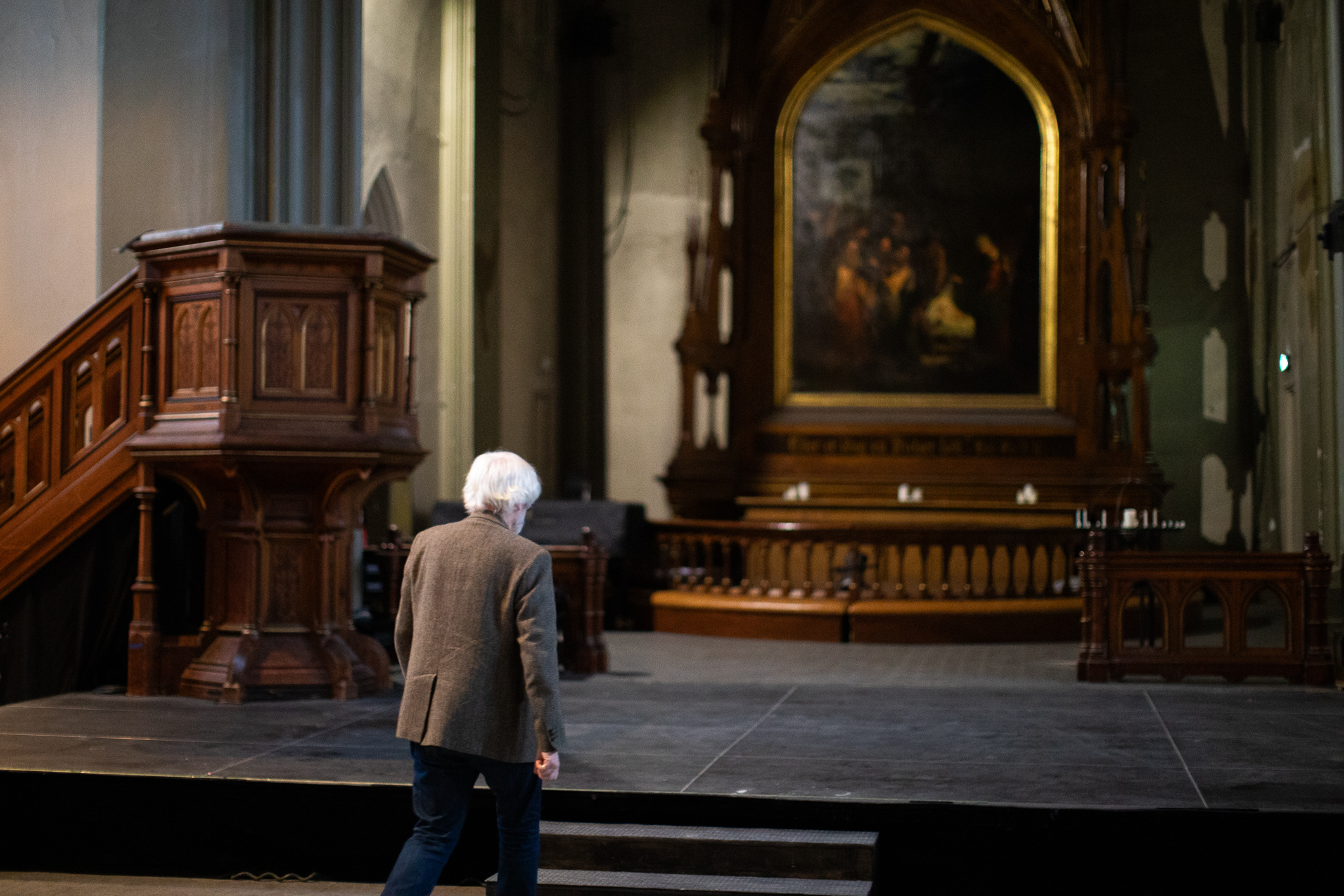 Gråhåret mann som går alene mot alteret i et stort kirkerom i brune toner.