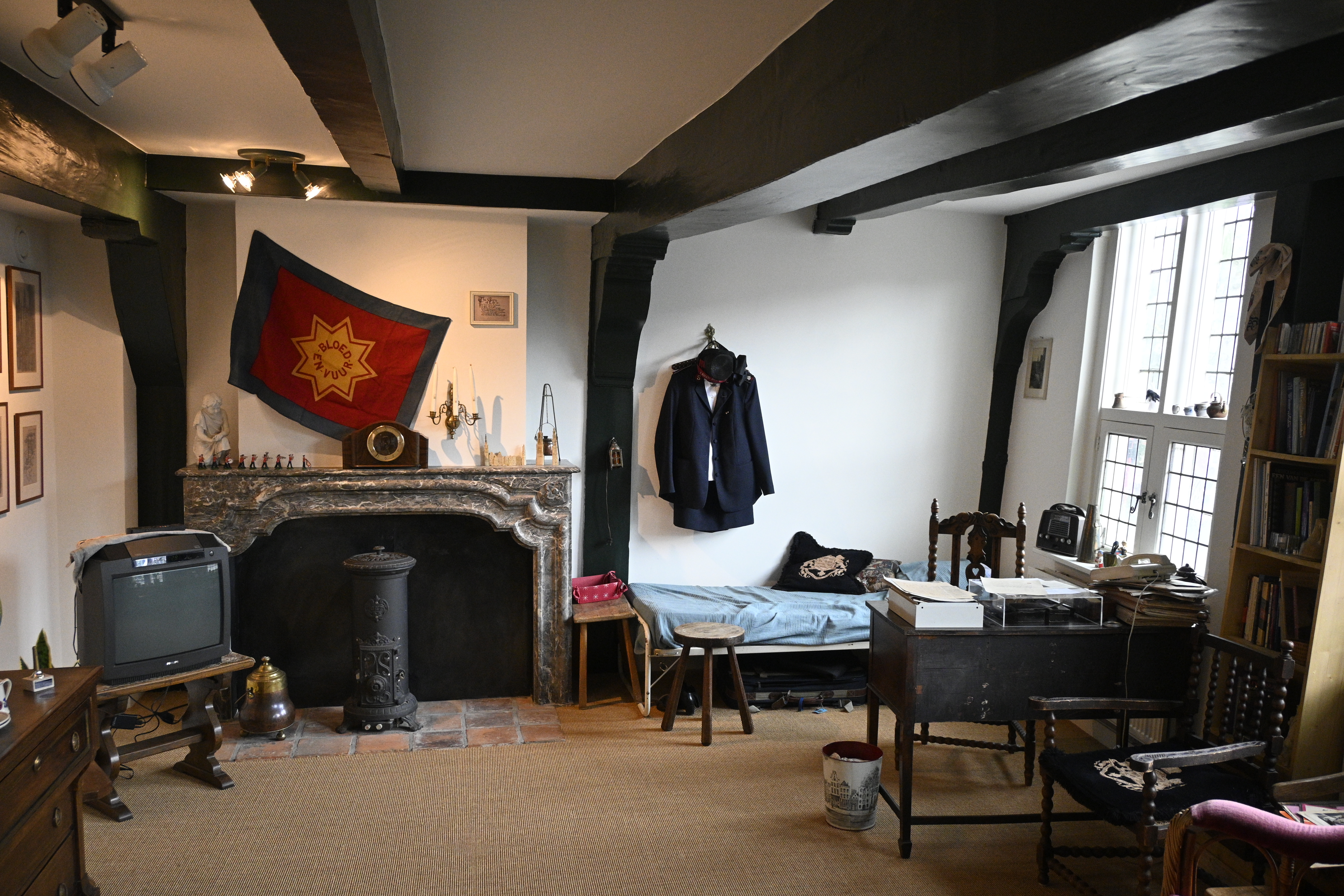Et rom med seng, TV, peis, skrivebord og kommode. Frelsesarmeens banner henger på veggen sammen med en mørk uniform og bonnett.