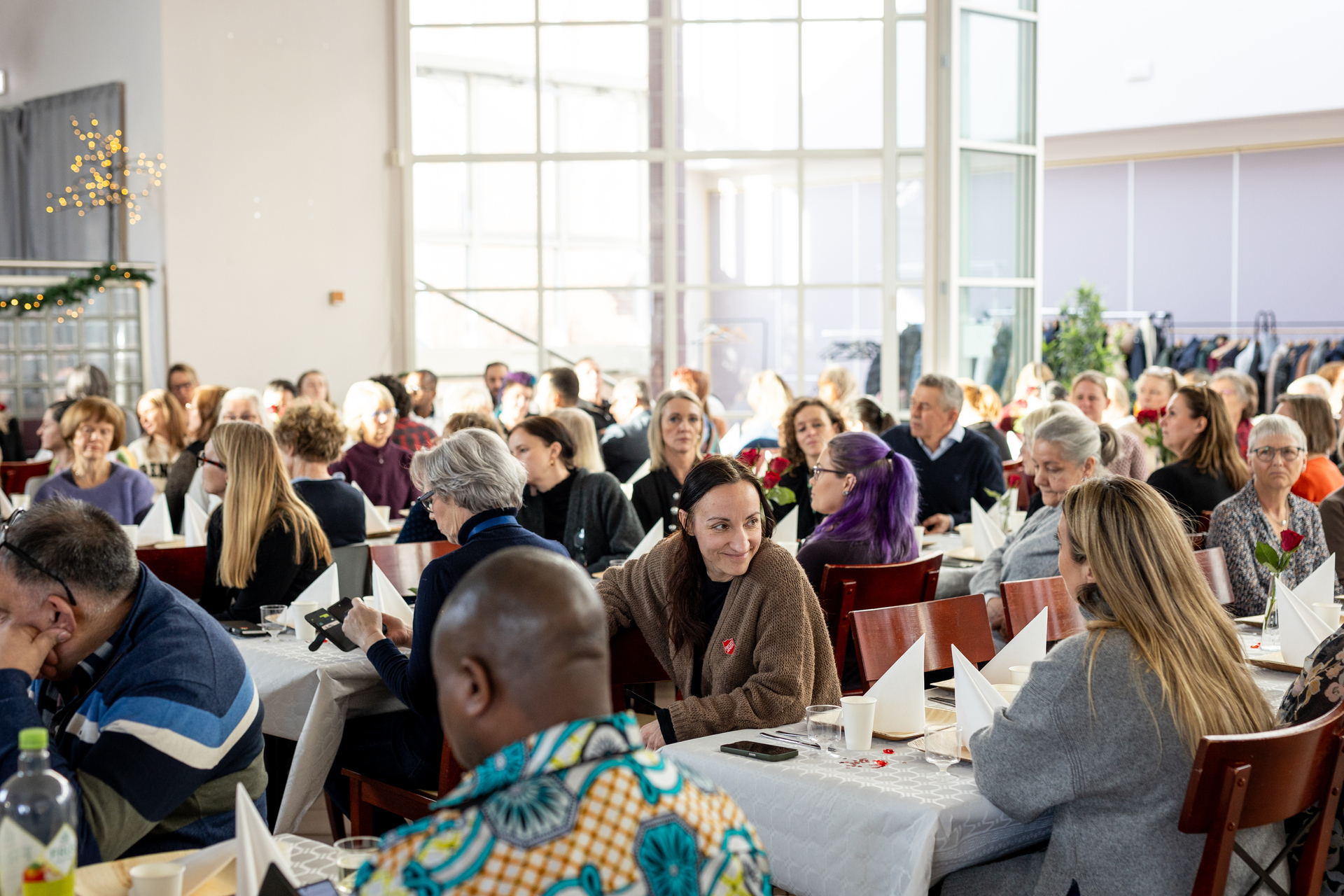 Foto: To sider etter hverandre. Begge viser mennesker ved flere langbord i en sal. Noen står på gulvet og klemmer hverandre.