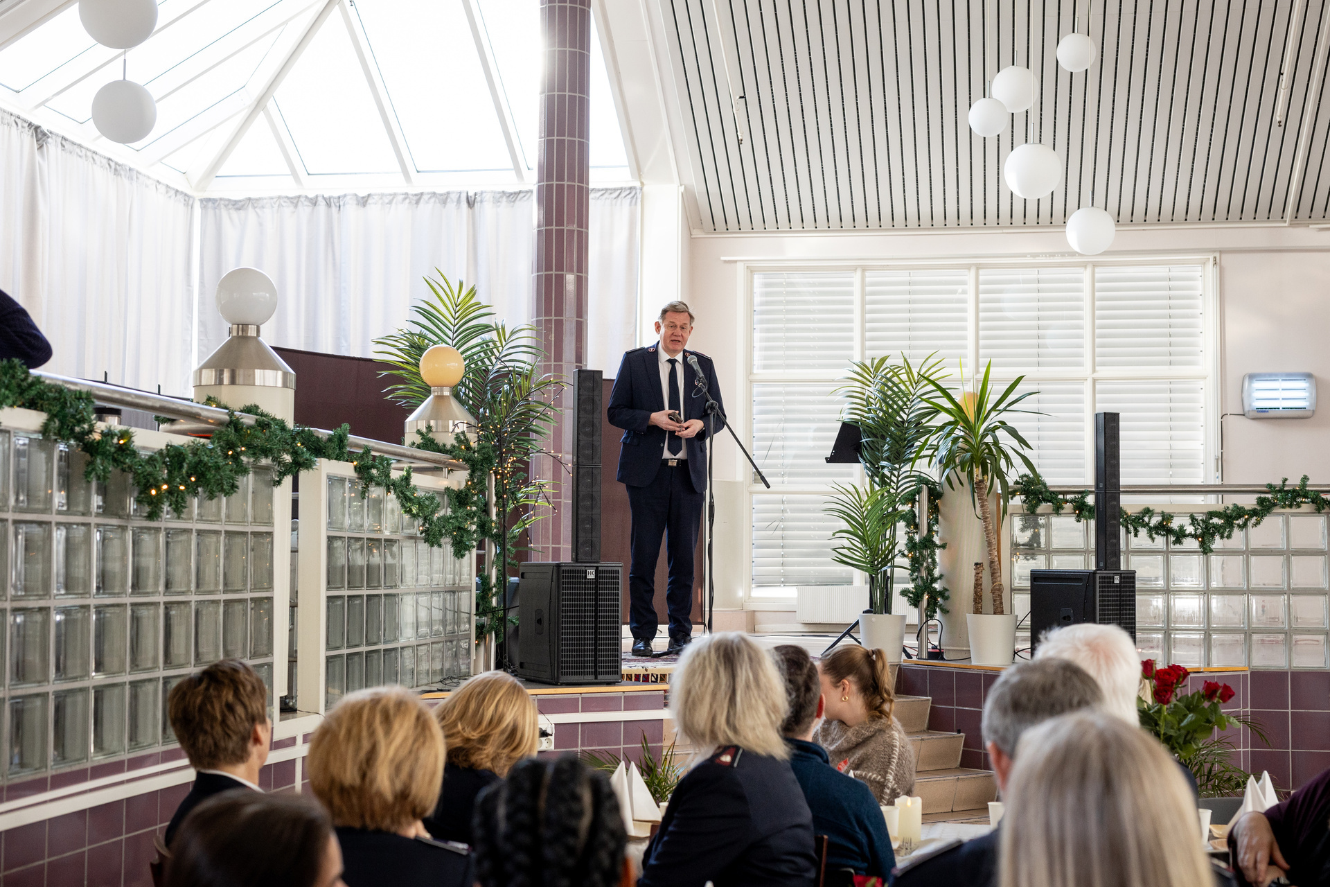 Foto: Mann i uniform fra Frelsesarmeen taler foran en gruppe mennesker som sitter til bords.