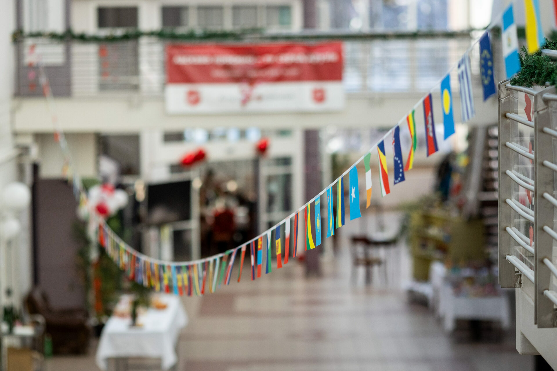 Foto: To bilder etter hverandre. Viser sammen store rom med glasstak høyt over – med og uten folk. På det første bildet er en lang rekke med flaggvimpler i fokus.
