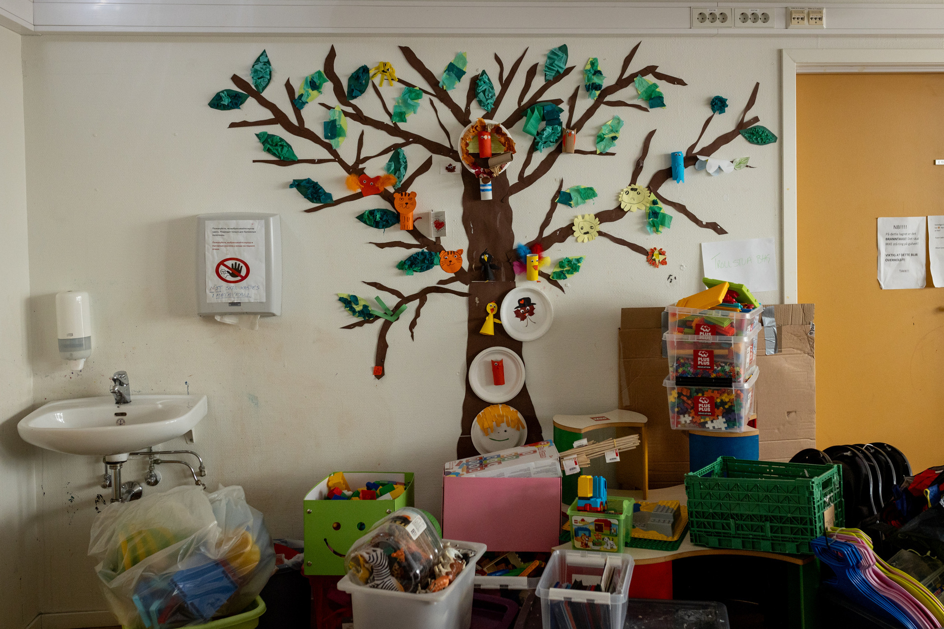 Foto: Rom med et tre med mange greier på veggen. Bladene er laget av fargerikt papir. På gulvet foran står mange esker med leker.