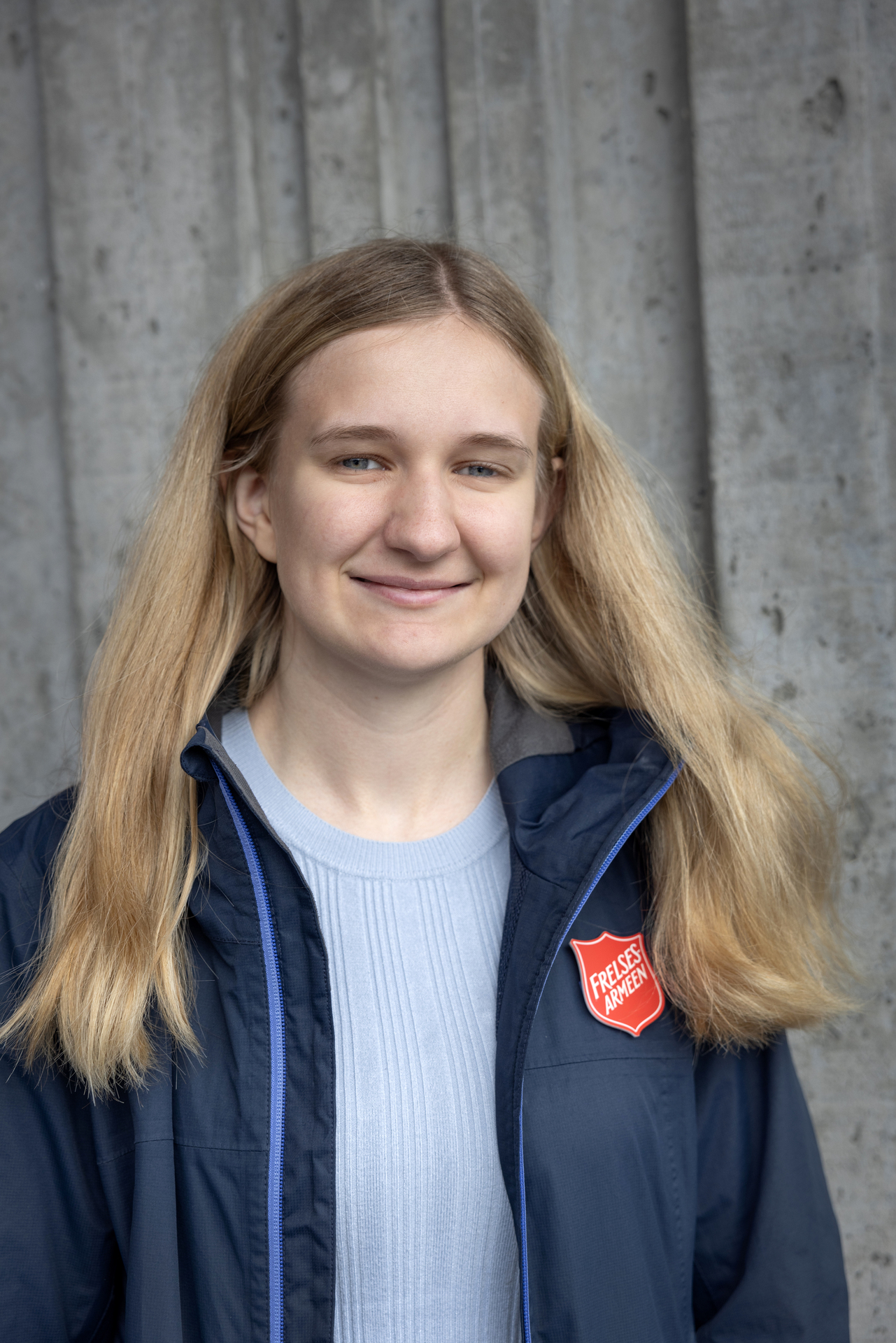 Foto: Kvinne med langt blond hår fra Frelsesarmeen i blå jakke med logo fra Frelsesarmeen på.