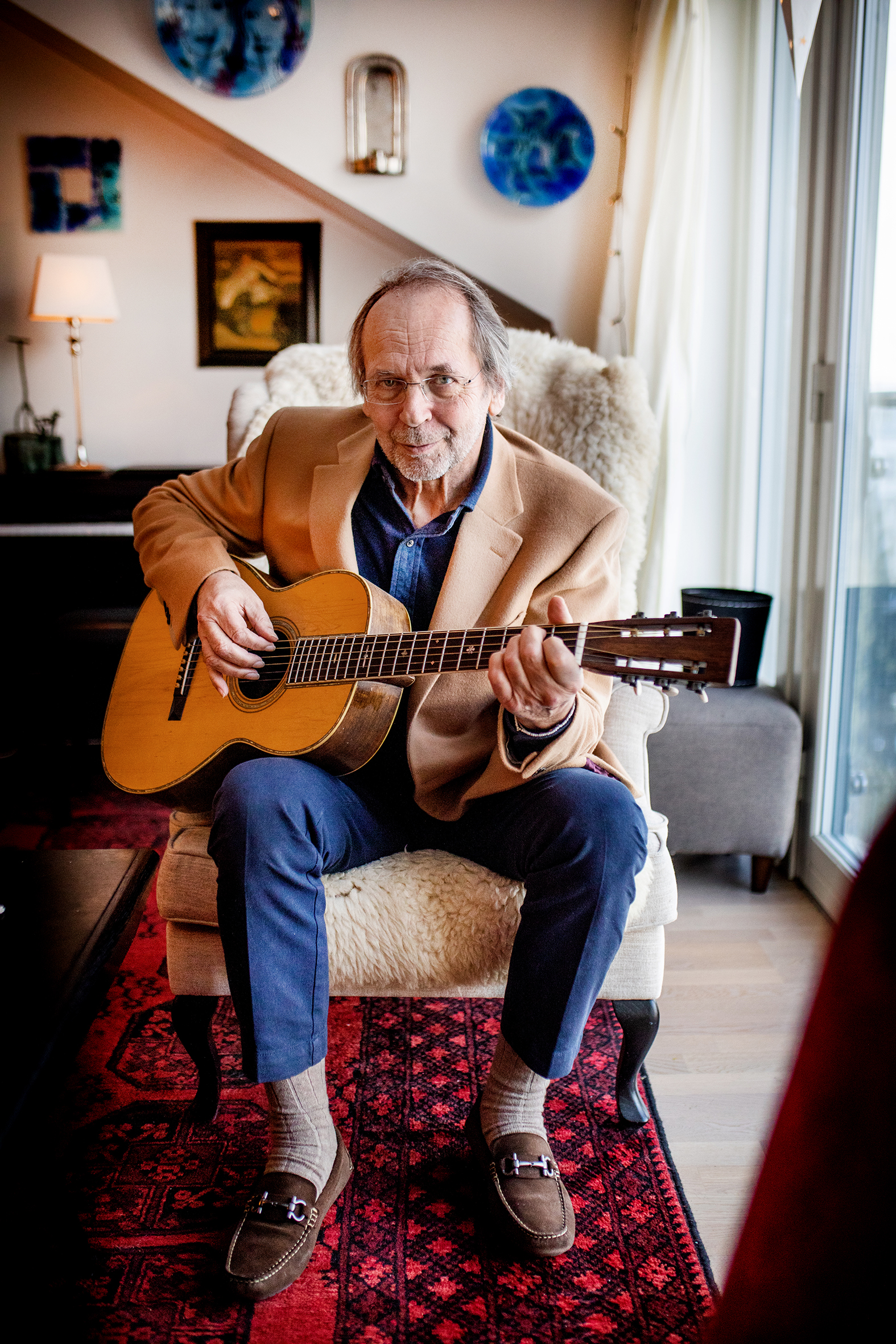 Ole paus sitter i sin egen stue og spiller på gitar (bilde t. v.). Ole Paus atår ute foran en vegg (bilde t.h)