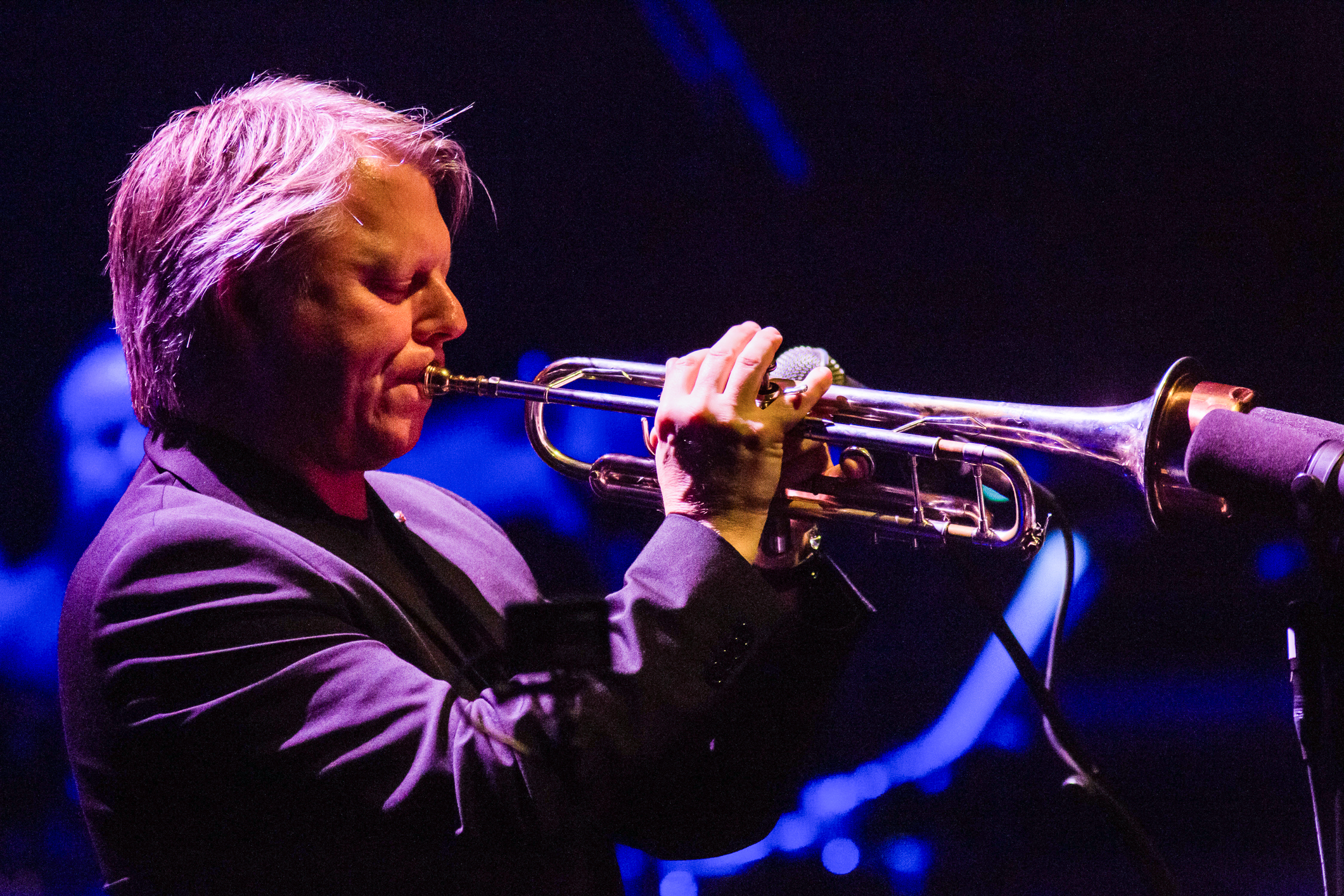 Mann som spiller trompet i blått scenelys. Øynene er lukket.