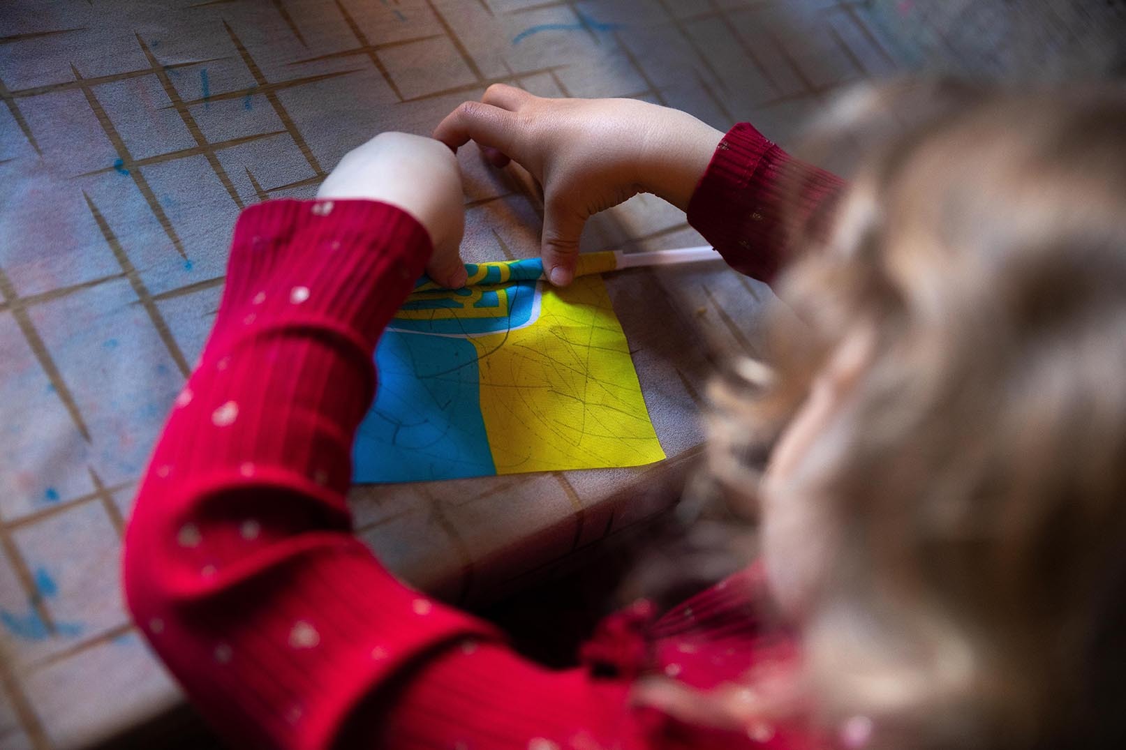 En liten jente med rød kjole ruller sammen et ukrainsk flagg.