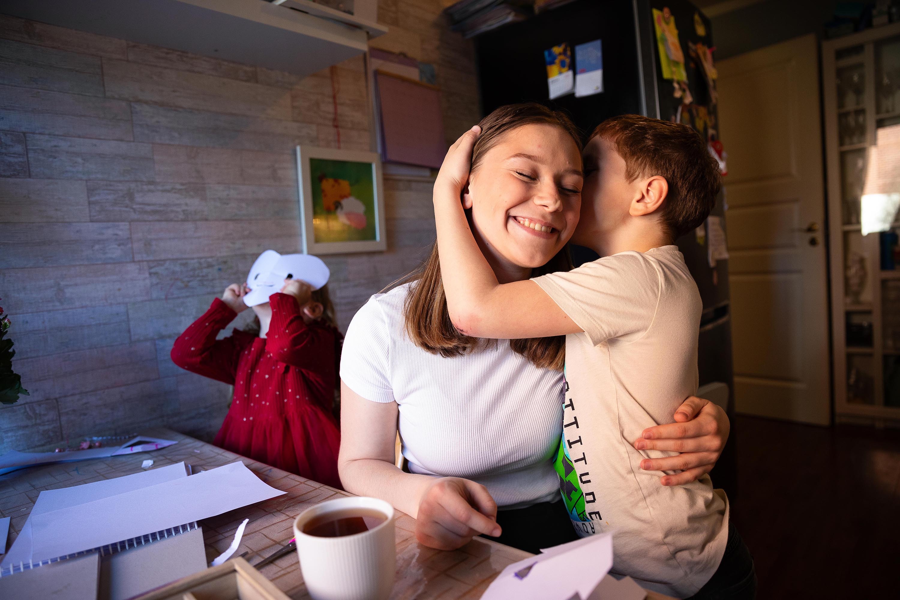 Ung jente klemmer en gutt. Bak leker ei lita jente med en papirmaske som er klippet som et hjerte