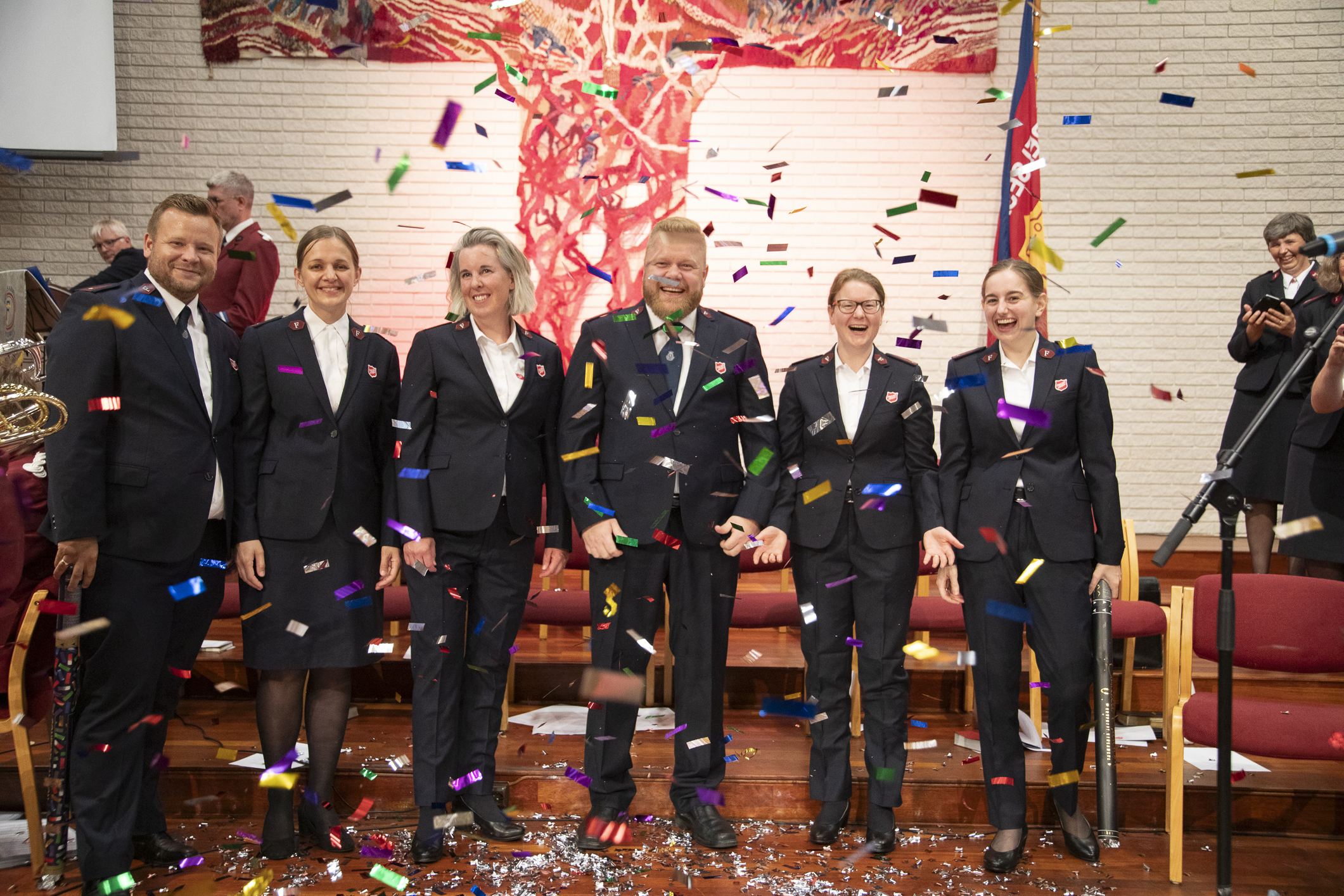 Seks mennesker i uniform står på rekke. Konfetti i luta rundt dem.