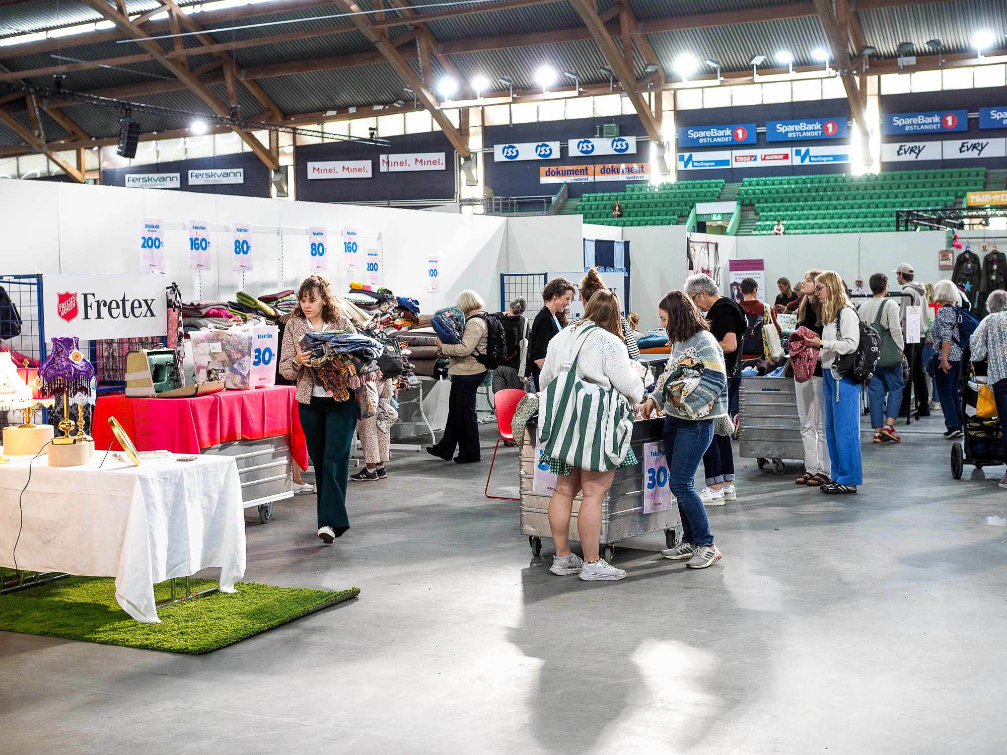 Stort område med klær og brukte klær og stoffer på bord og i kasser. Folk plukker ut ting de vil bruke til å sy om til noe nytt.