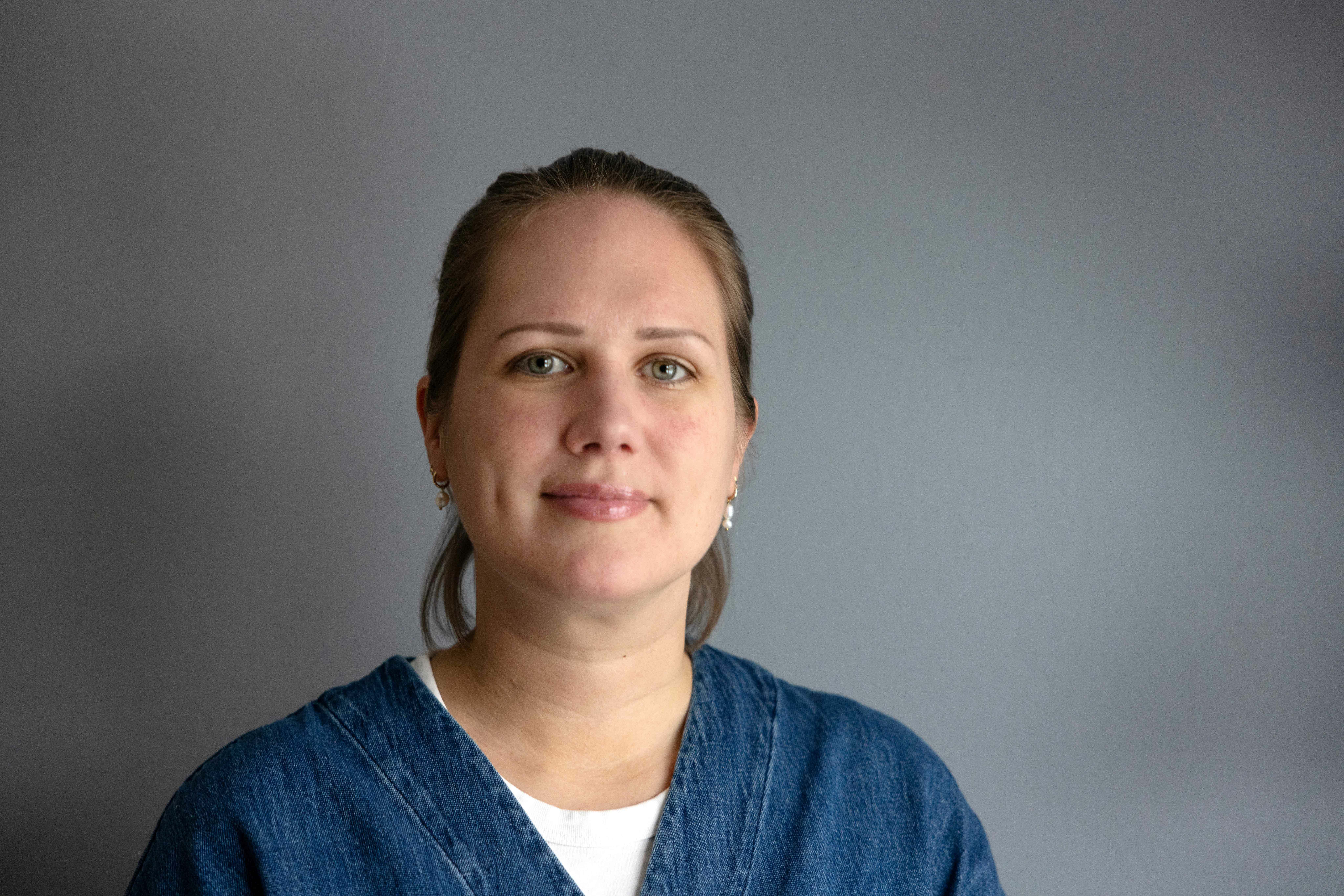 Ung kvinne med året bakover med blå dongerisskjorte  og hvit t-skjorte inni. Vegge bak er grå.