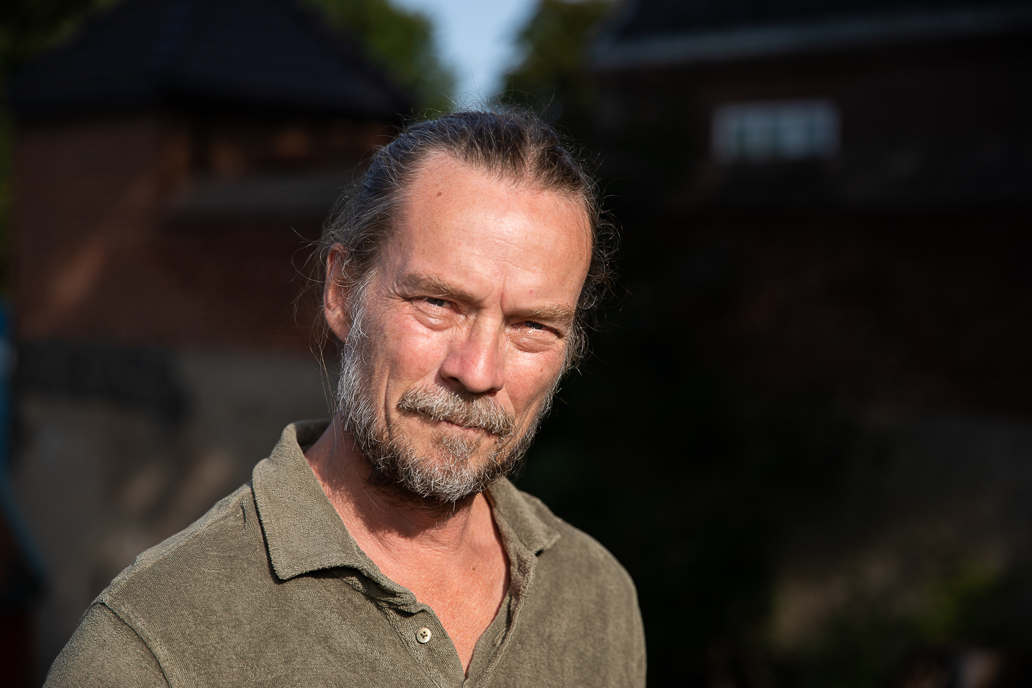 Solbrun mann med hestehale og skjegg ser inn i kamera. Fotografert fra skuldrene og opp.