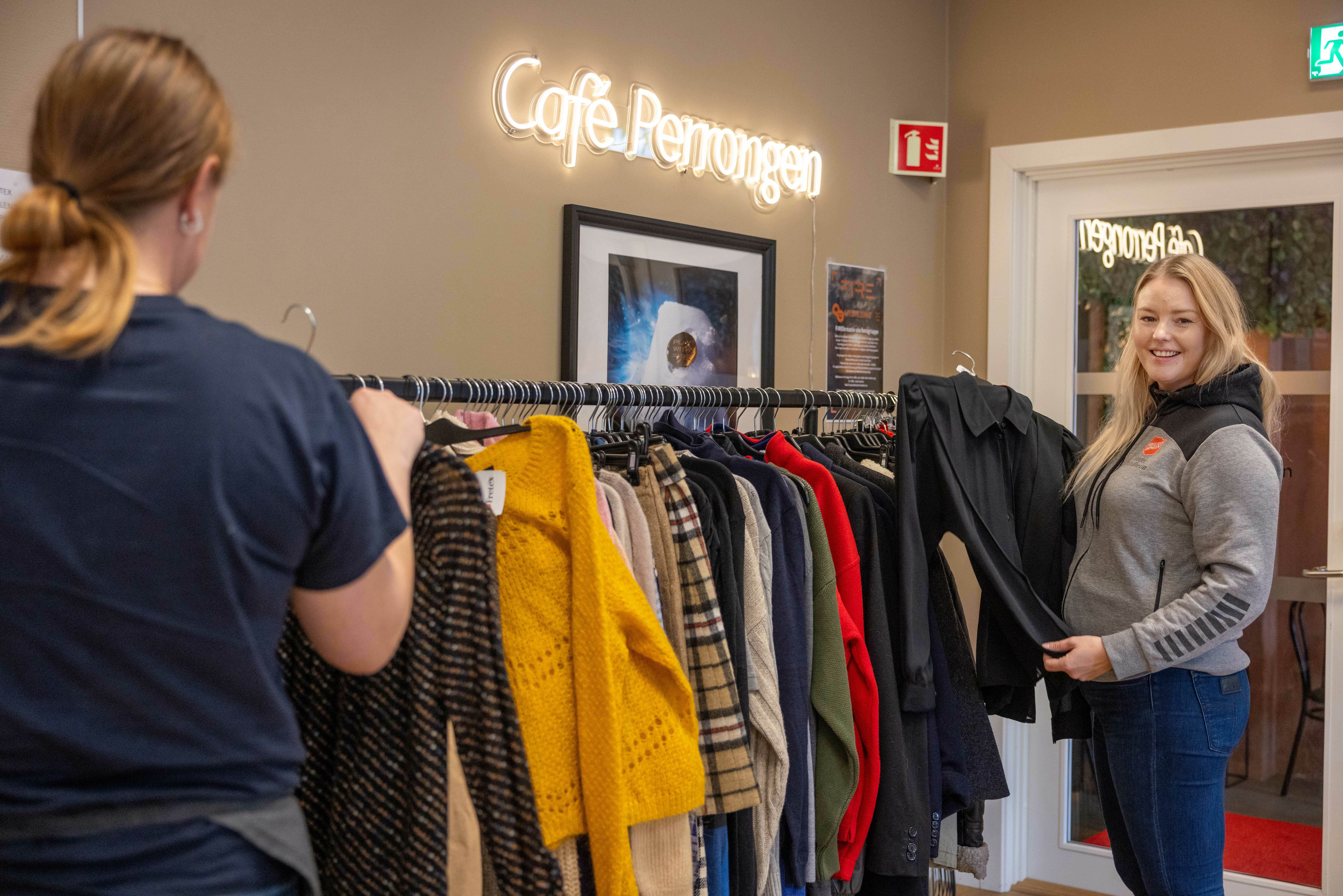 To kvinner henger klær på et stativ.