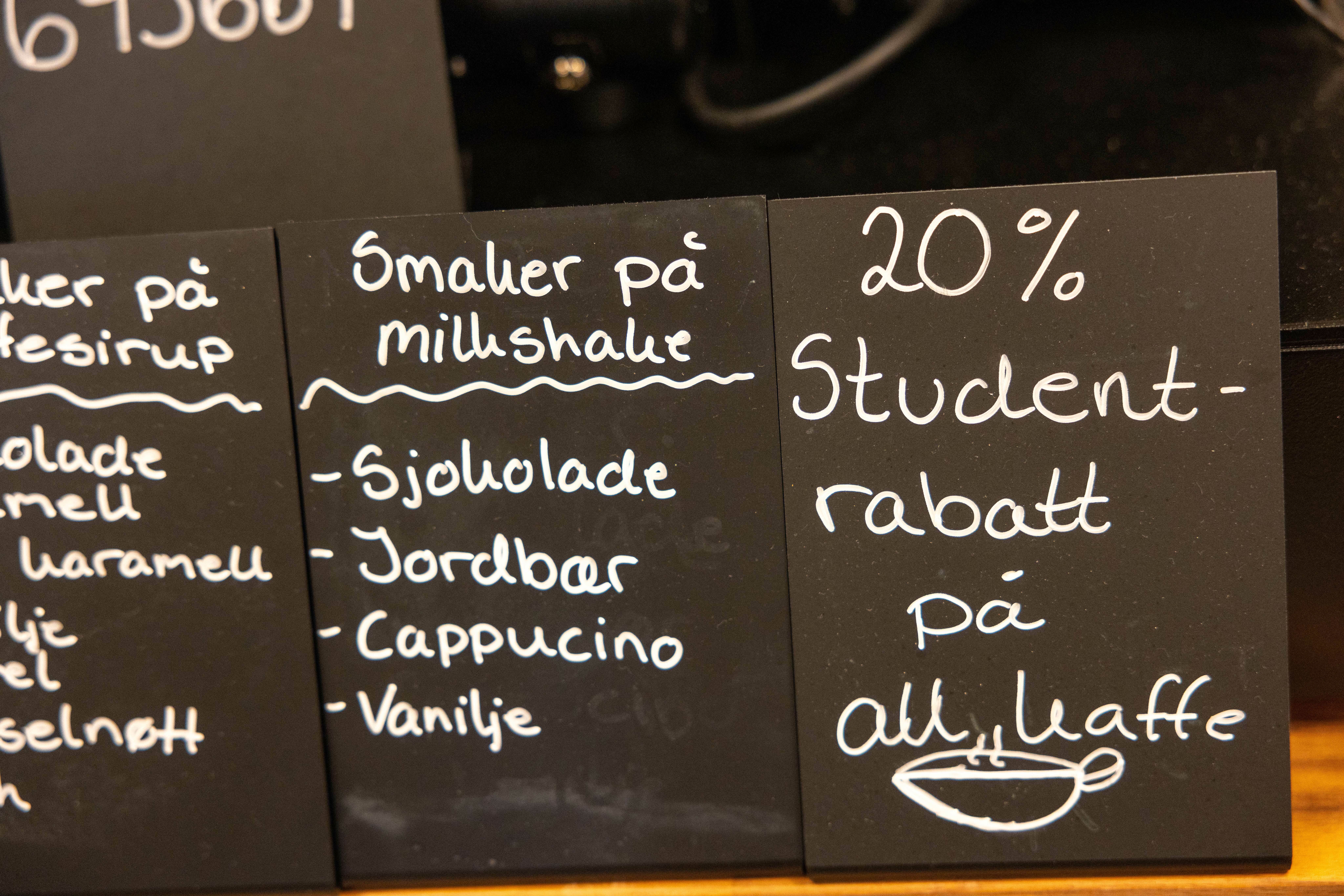 Sort menytavle med hvit skrift der det står håndskrevet: 20% studentrabatt på all kaffe.