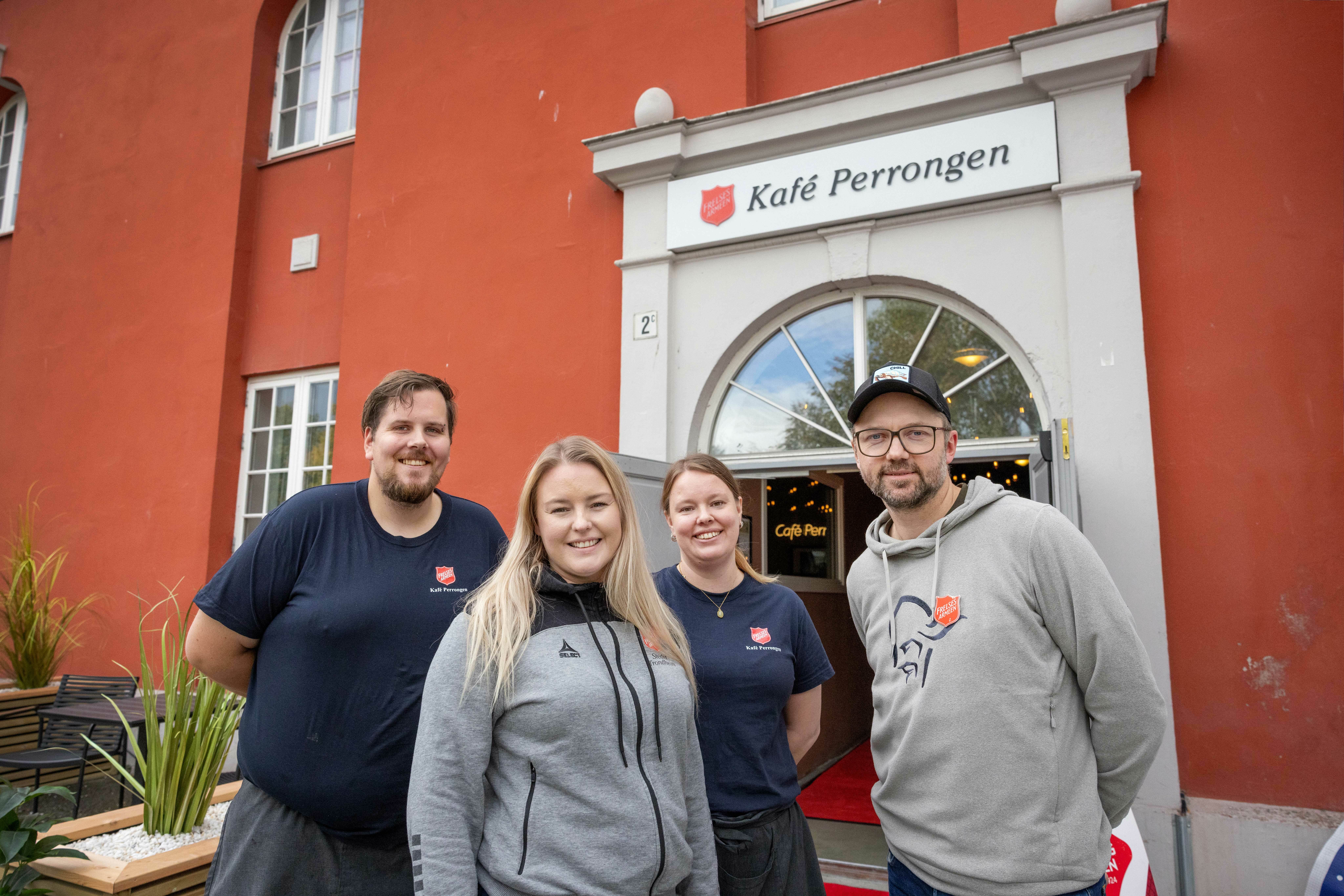 Fire personer står utenfor en rød murbygning. Over inngangsdøren står det Kafé Perrongen.