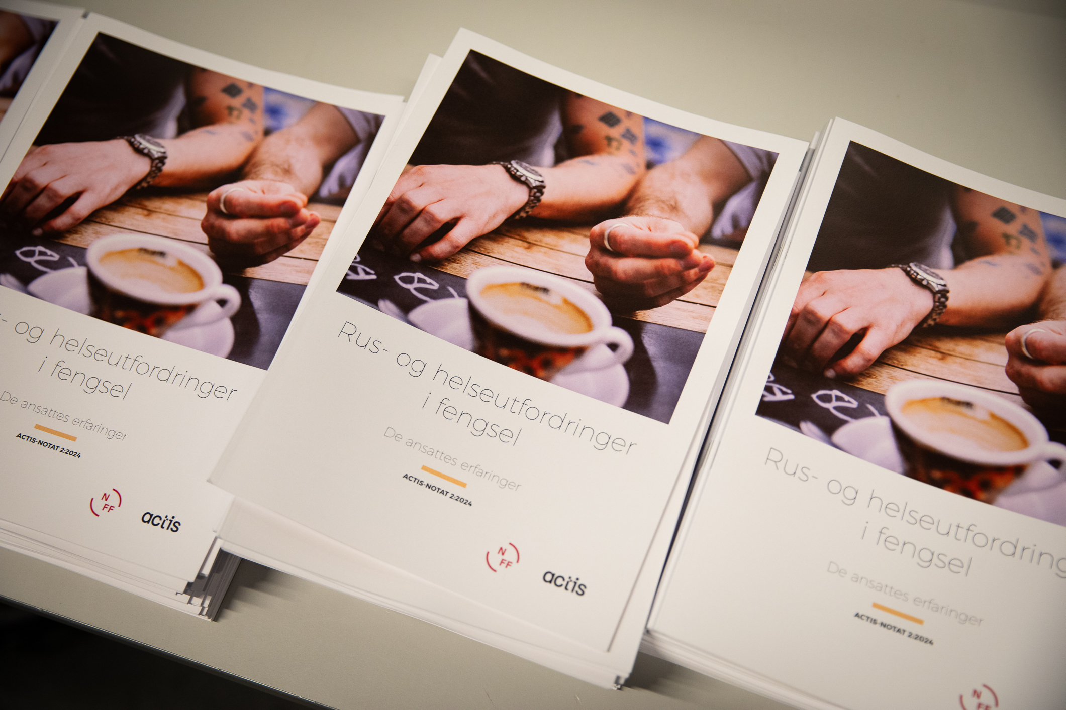 Foto: Tre bunker med en rapport. Bildet på fronten er av to tatoverte armer – fra to menn – og en kaffekopp.