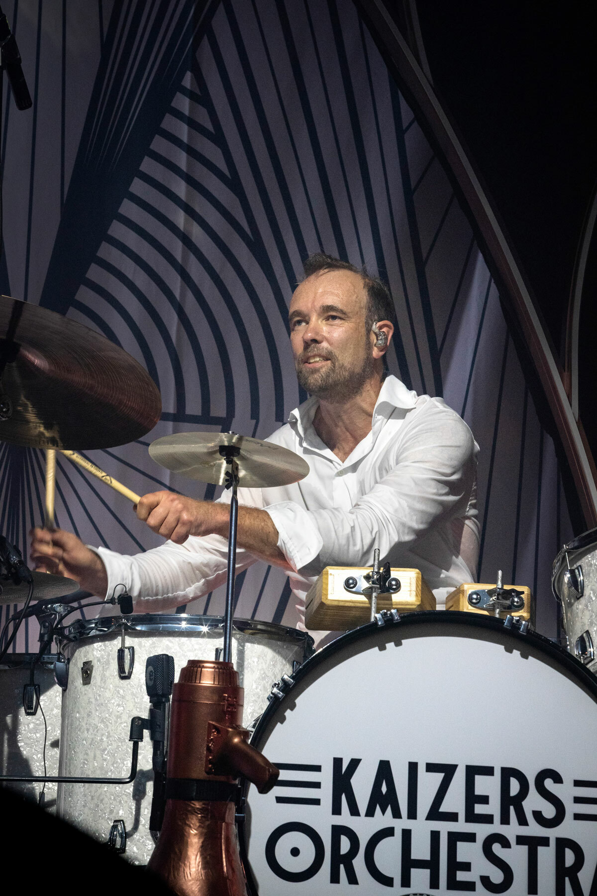 Foto: Mann med mørkt hår og skjegg spiller på et trommesett. det står Kaizers Orchestra på stortrommen.