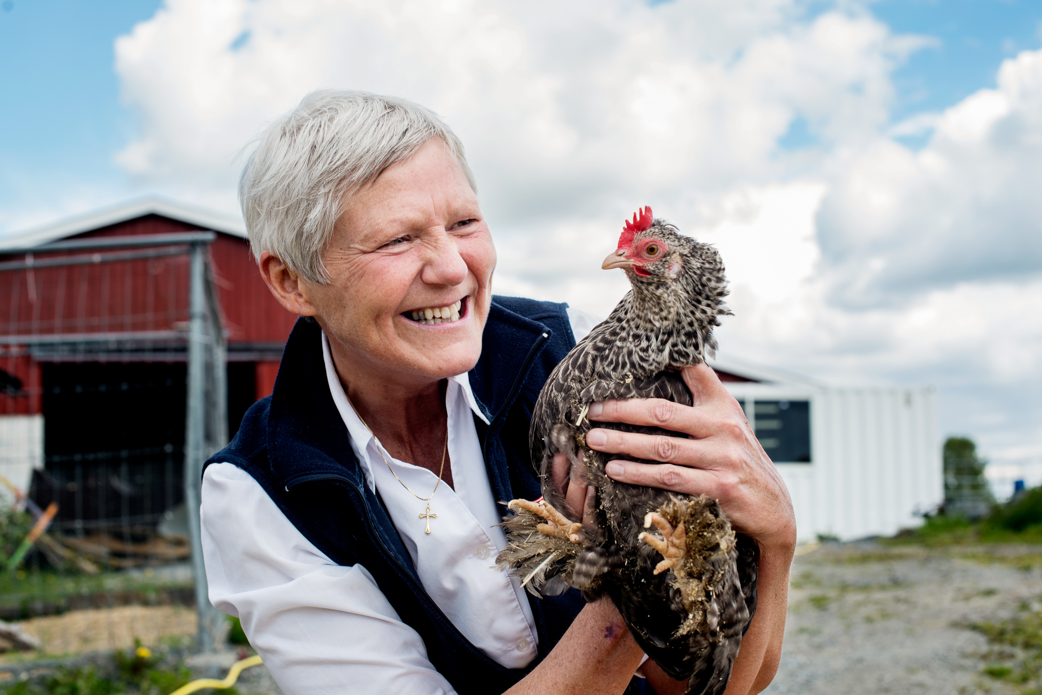 Dame som holder en høne ute i friluft. I bakgrunnen sees en låve.