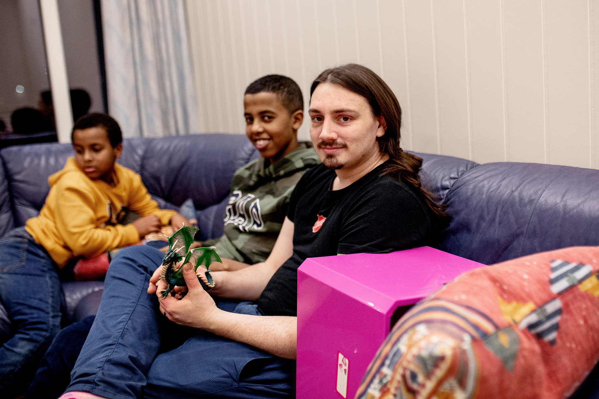 Bildet viser en mann med langt, brunt hår og svart t-skjorte med frelsesarme-skjold. Han sitter i en sofa sammen med to gutter, den ene smiler mot kamera, mens den andre er opptatt av noe utenfor bildet,