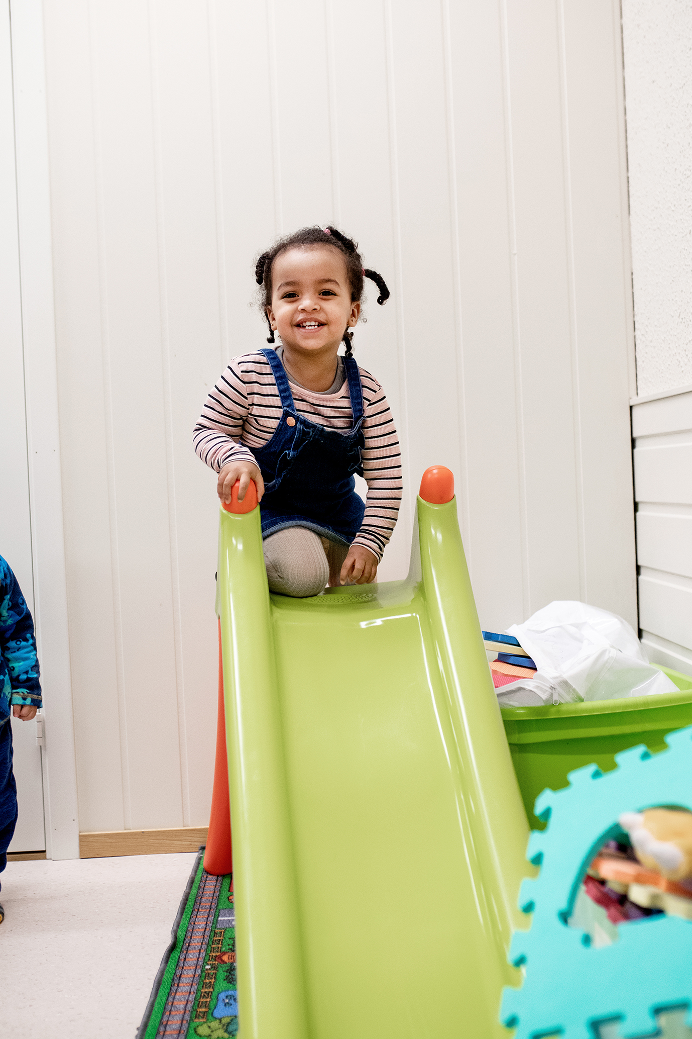 Det flrste bildet viser en gutt som tegner et hus. Det andre bildet viser en smilende jente som sitter på toppen av en grønn plastsklie.