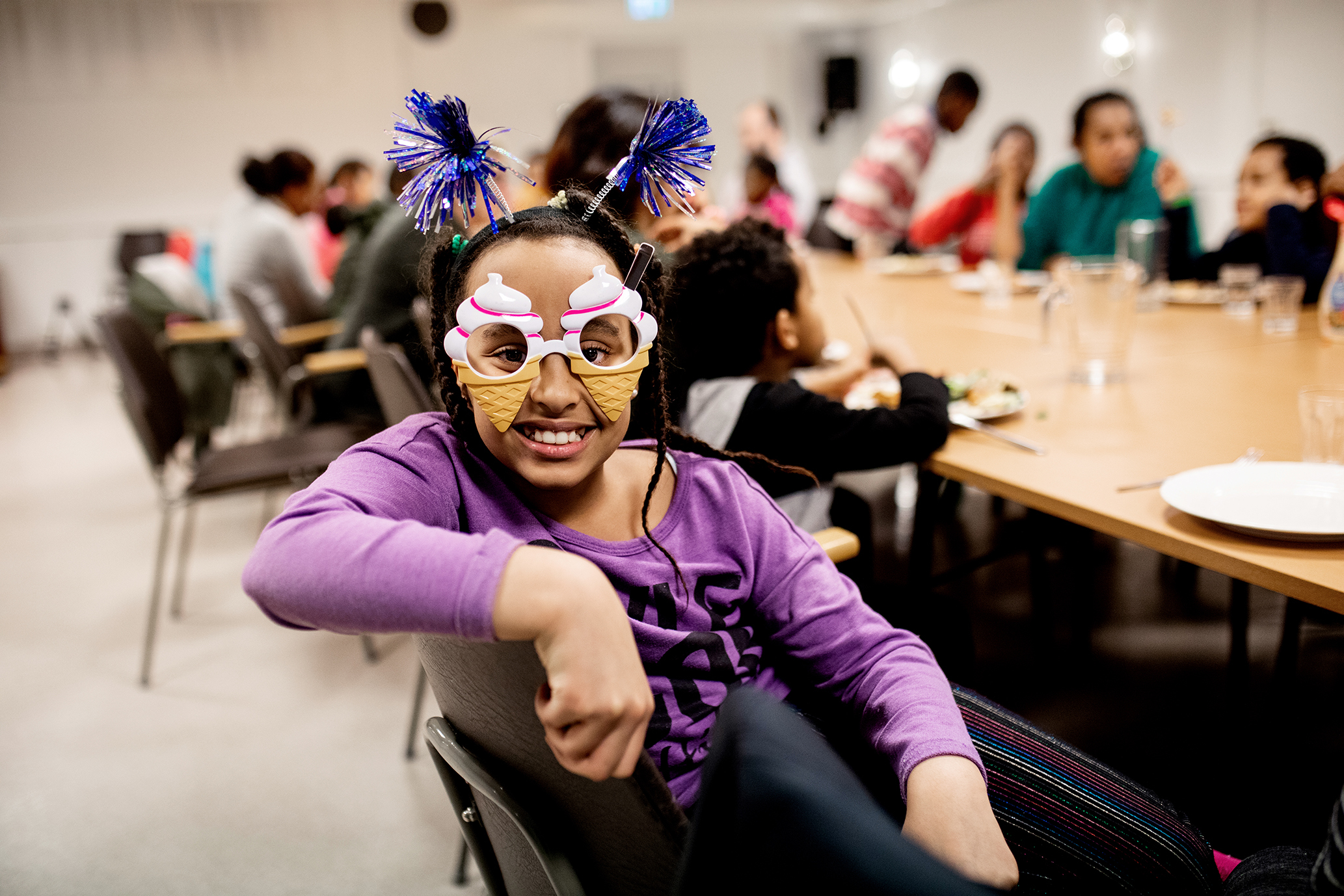 Bildet viser ei jente med lilla genser som sitter og smiler mot kamera. Hun har på seg en maske formet som to is i kjeks.