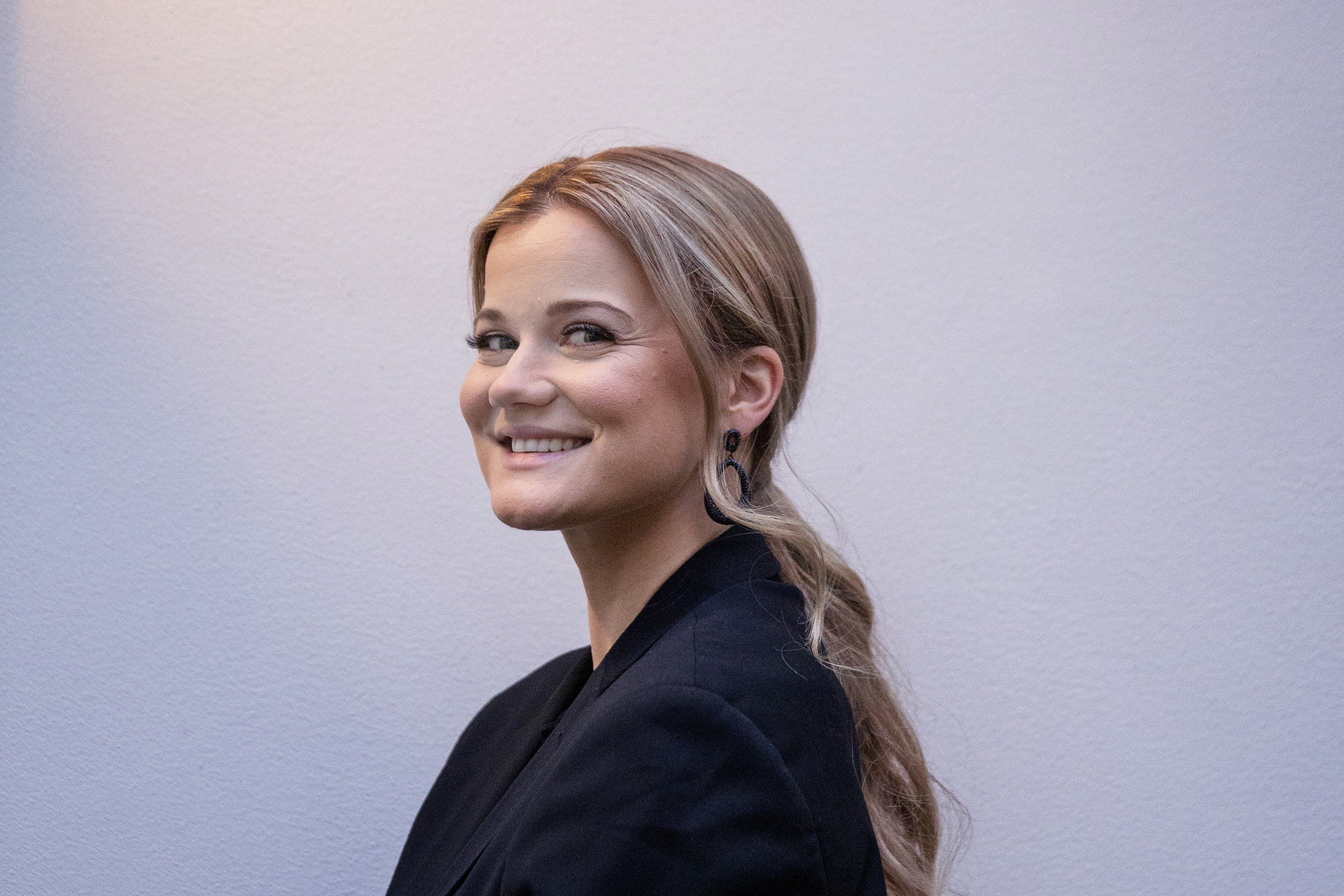 Nærbilde av Sandra lyng som står mot siden foran en hvit vegg.