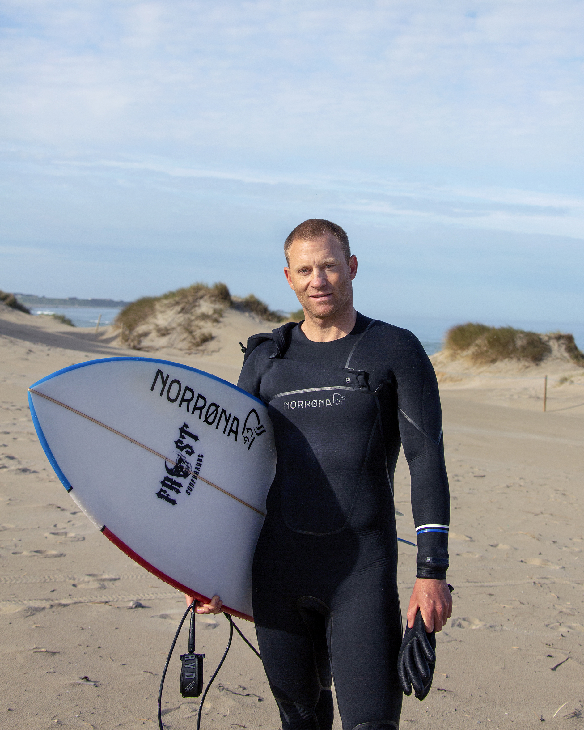 Shannon står og ser inn i kamera, med surfebrettet under armen.