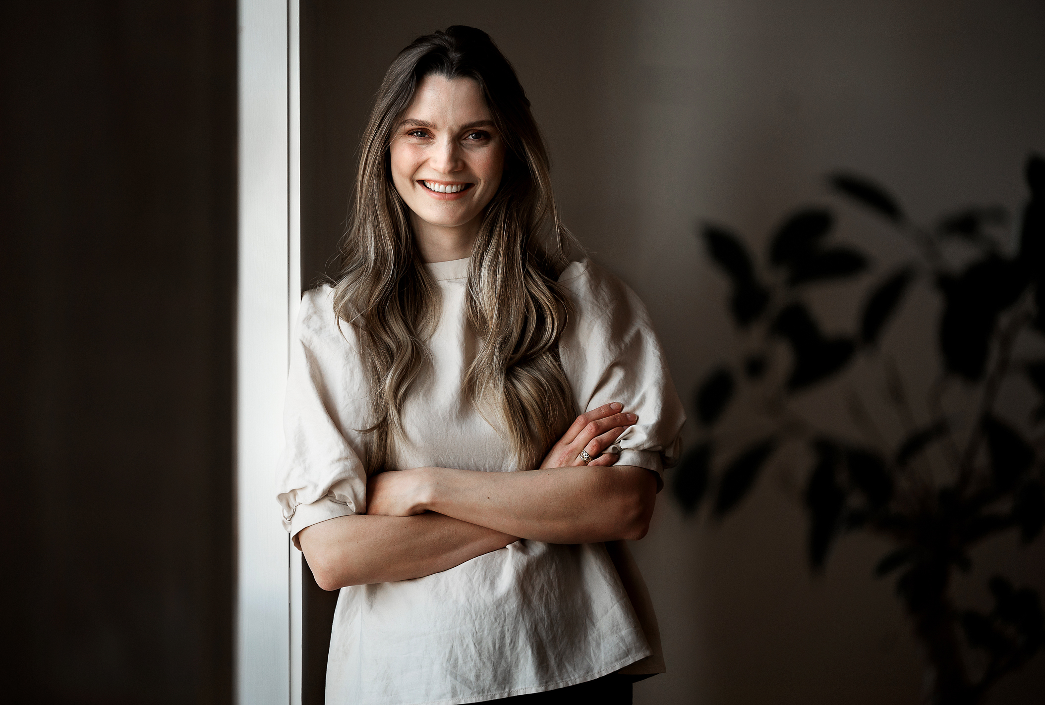 Foto: Kvinne med langt, mørkt hår og lys topp står oppstilt foran kamera. Smiler.