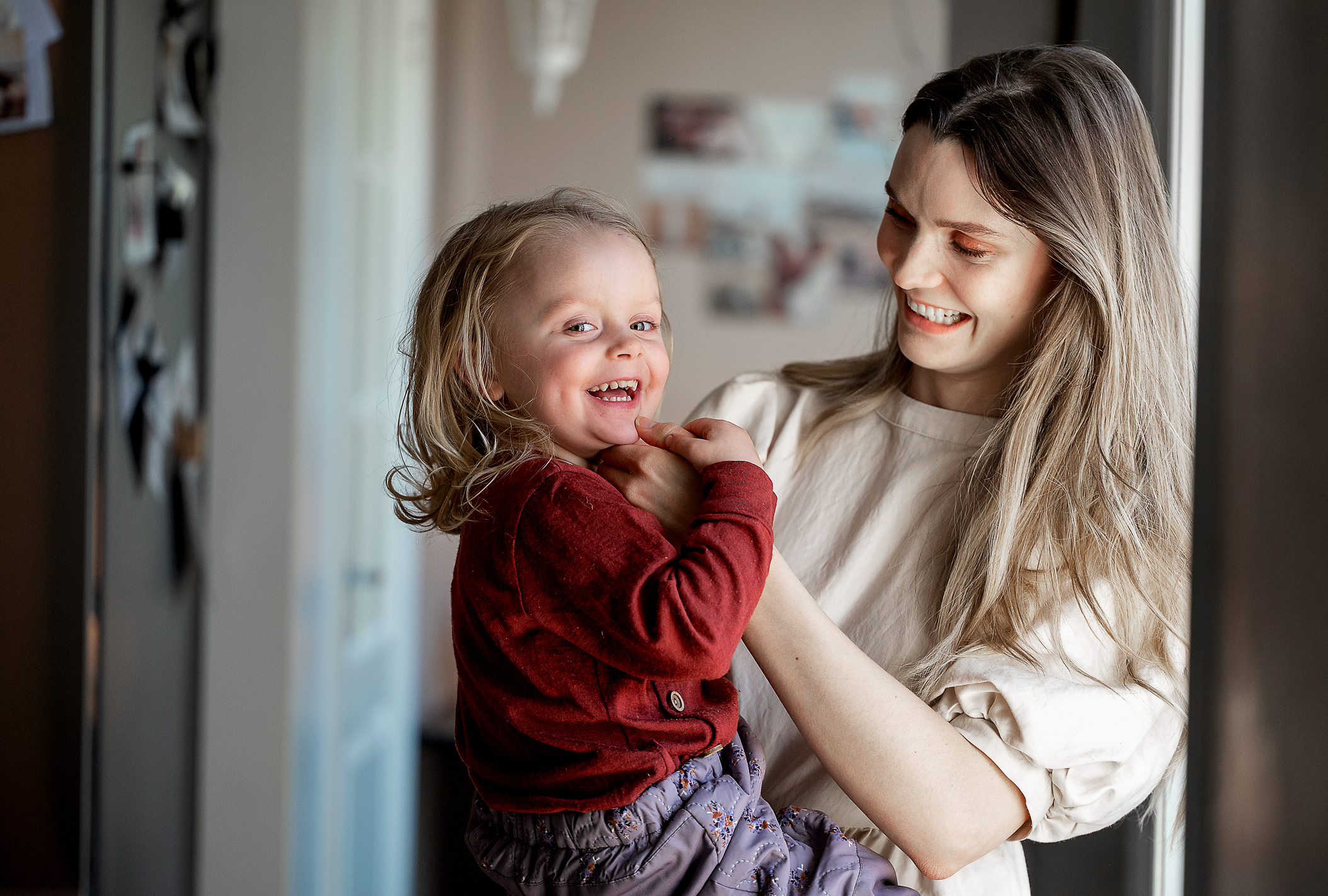 To foto av mor og datter på kjøkkenet. Treåringen ser inn i kamera og ler på begge bildene. Moren ser på datteren.
