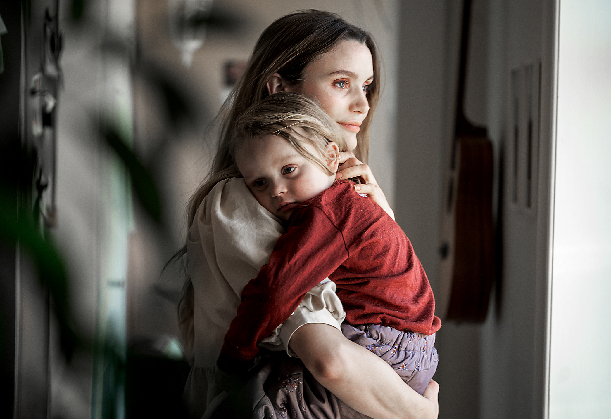 Foto: Ung mor med langt, mørkt hår holder en liten jente på rundt tre år i sine armer. Den lille er lys i håret.