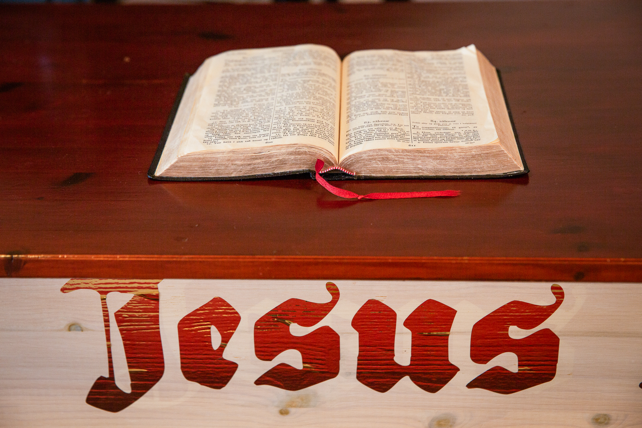 En oppslått bibel ligger på et alter. Under står det malt Jesus med store, røde bokstaver i gotisk skrift.