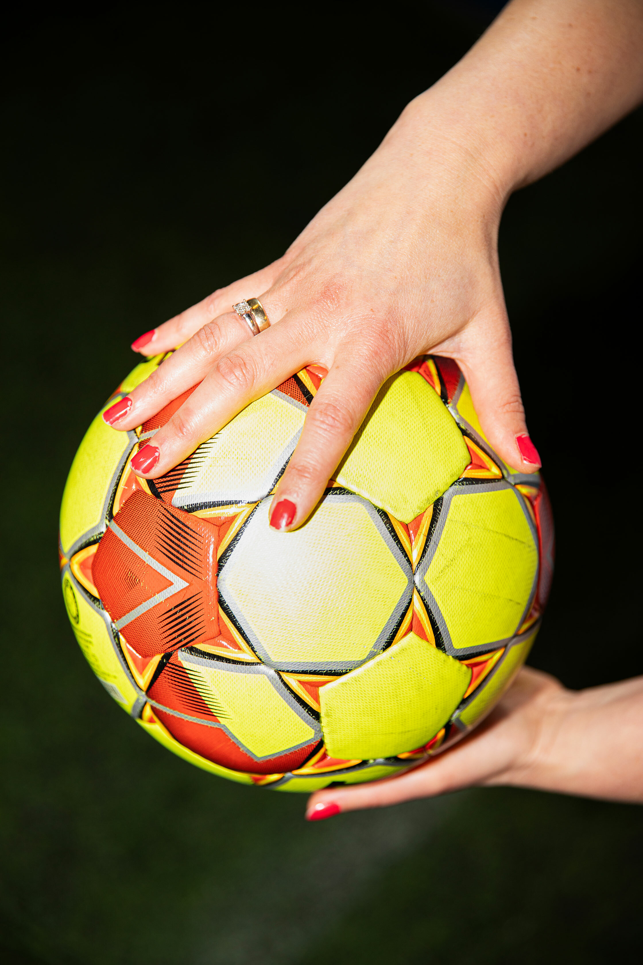 Foto: Nærbilde av en fotball i gult og rødt. Holdes av to kvinnehender.