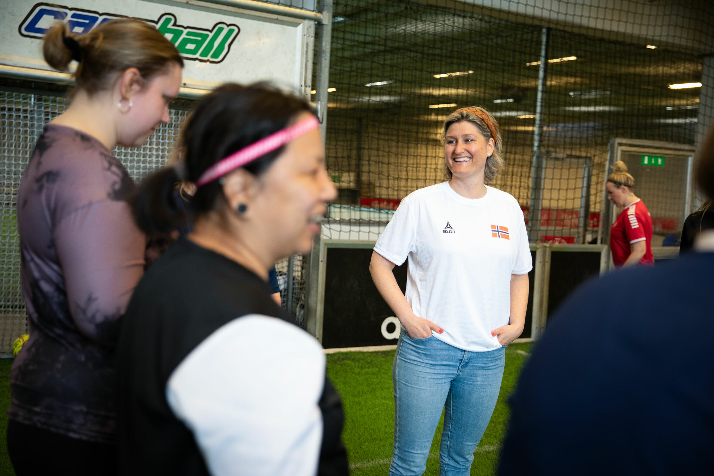 Foto: Kvinne i hvit T-skjorte som snakker med flere fotballspillere.